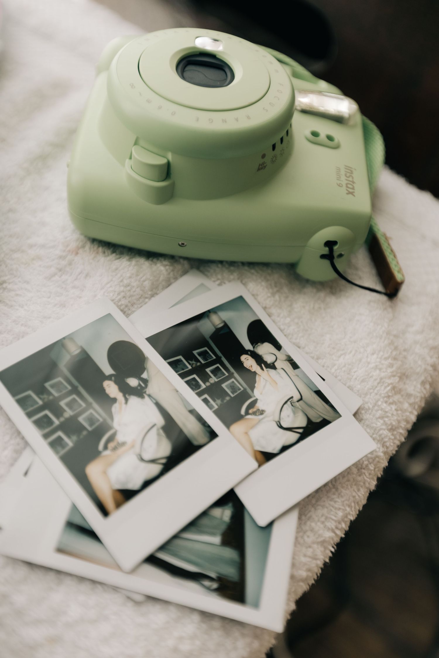 Mint green instant camera next to scattered polaroid photos on white fabric.