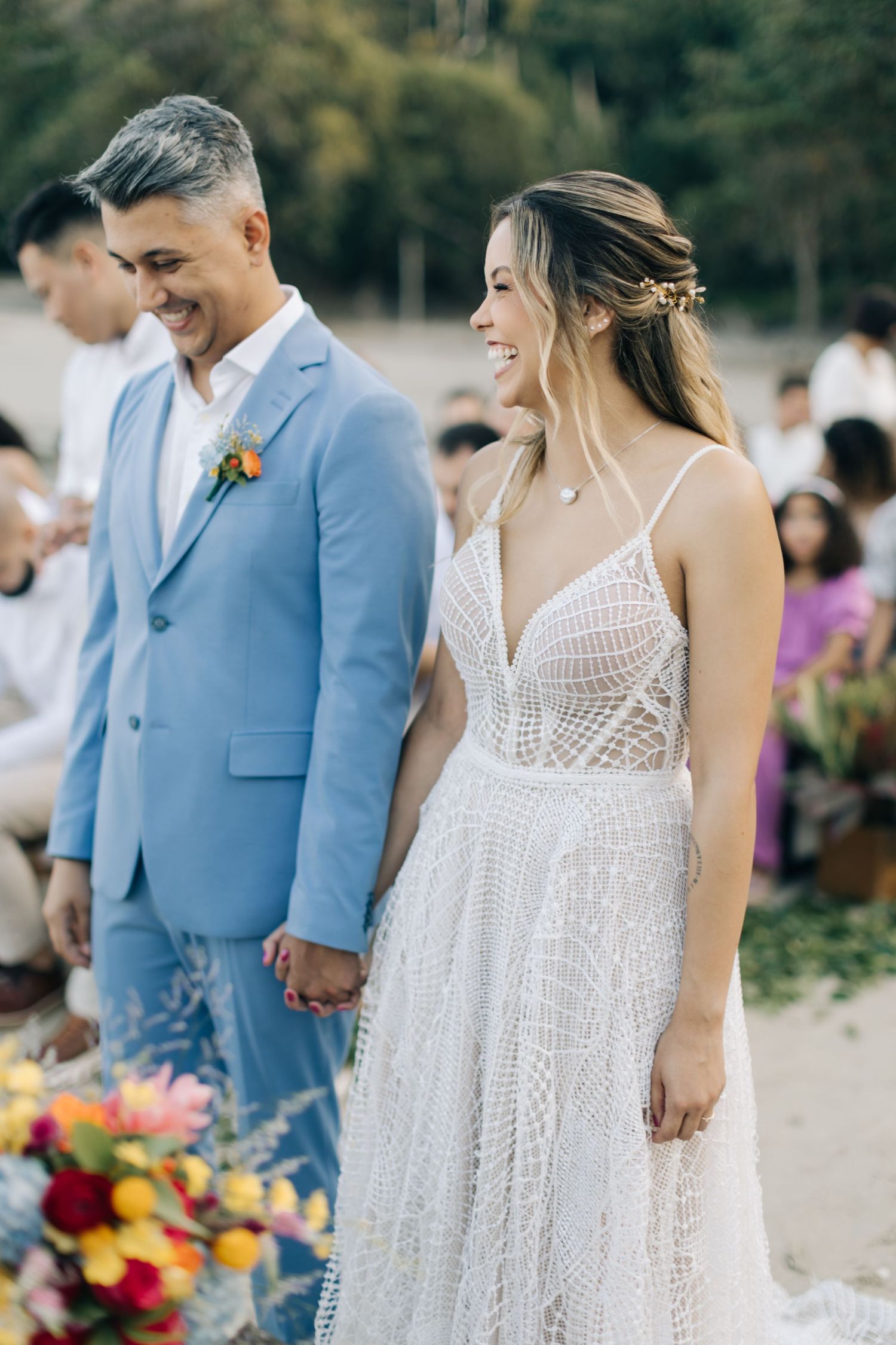 Joyful outdoor wedding scene with couple in light blue suit and detailed white lace gown.