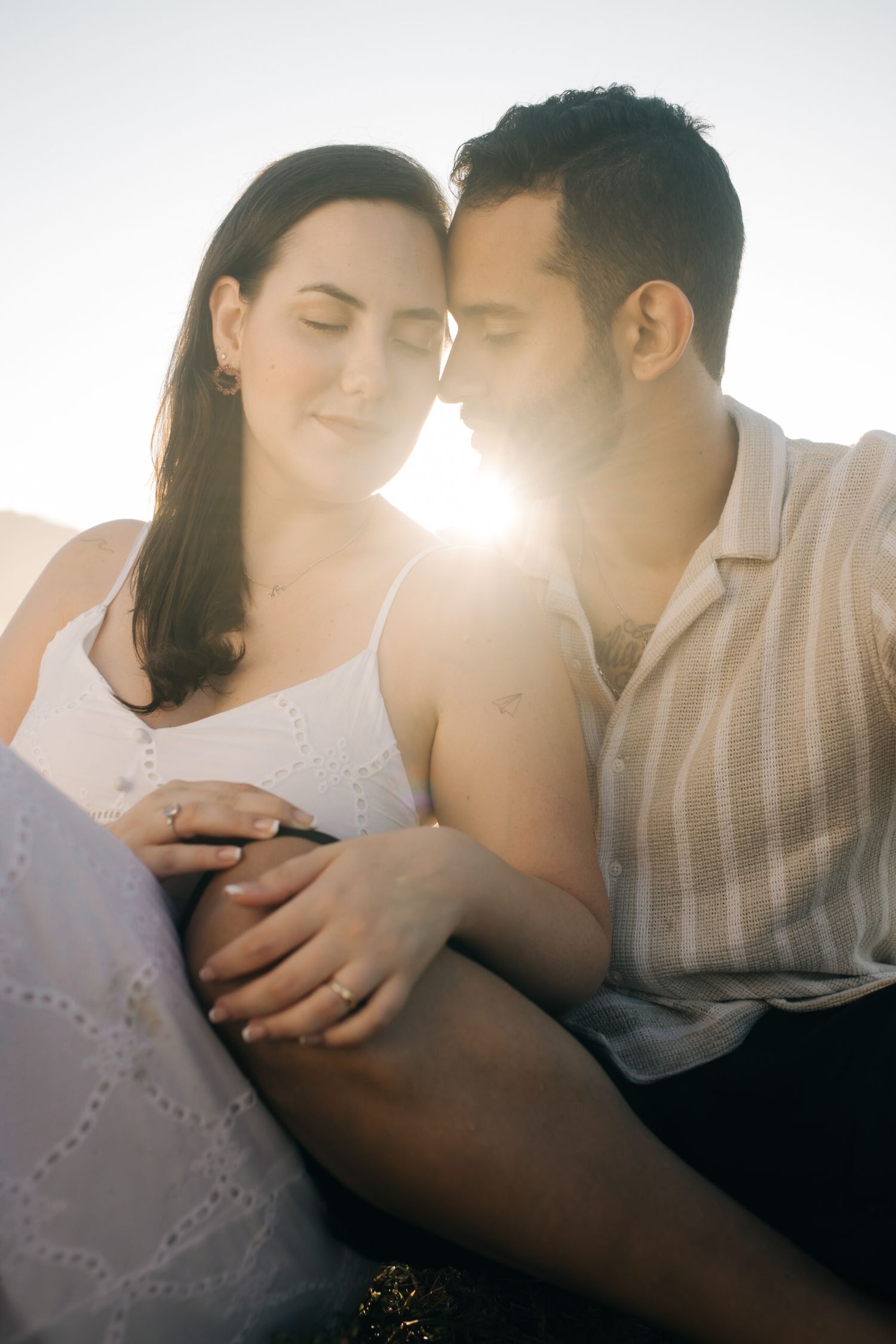 Sunlit close-up of couple sharing tender moment during outdoor photoshoot.