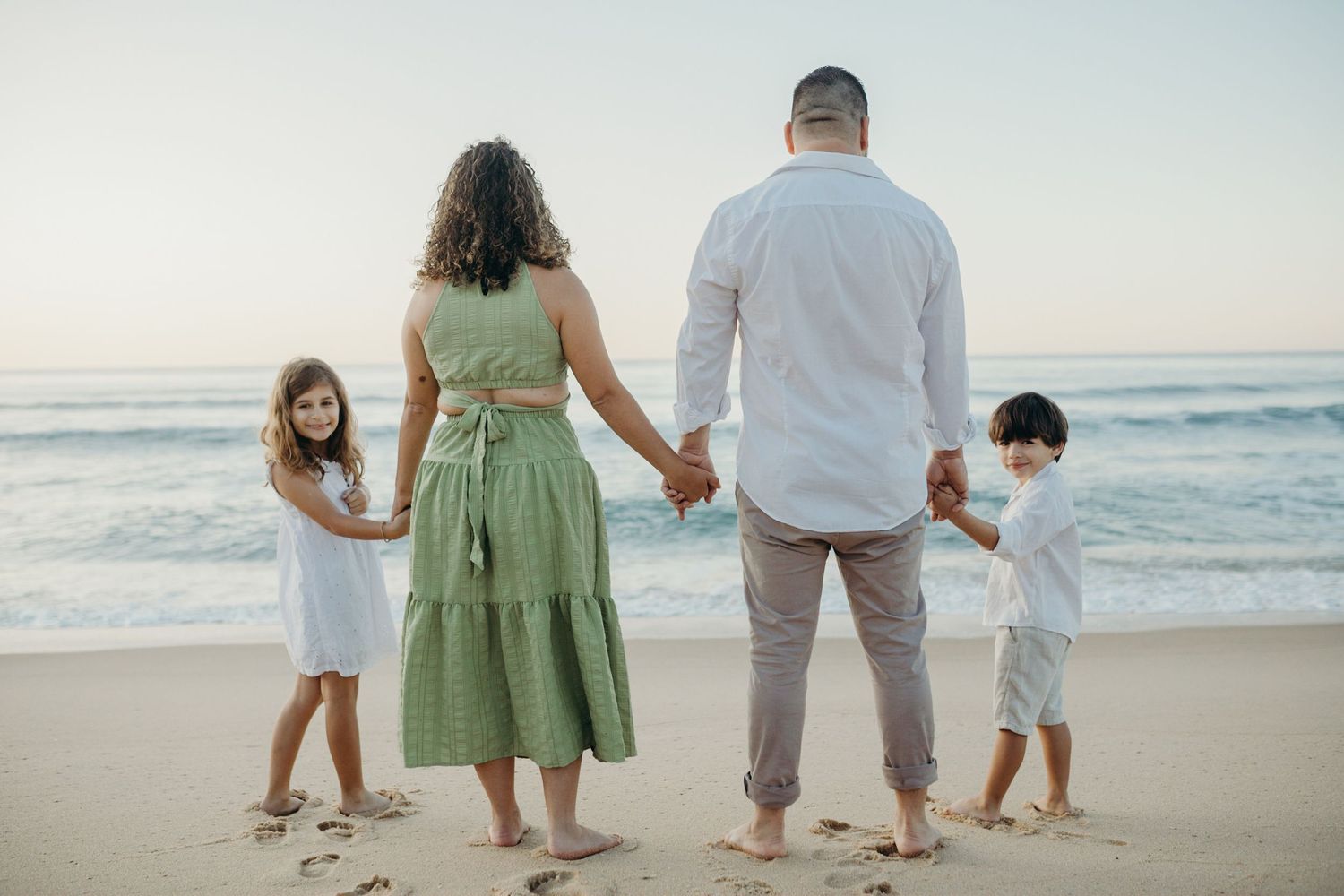 A family holding hands while standing together on a misty beach at sunset.