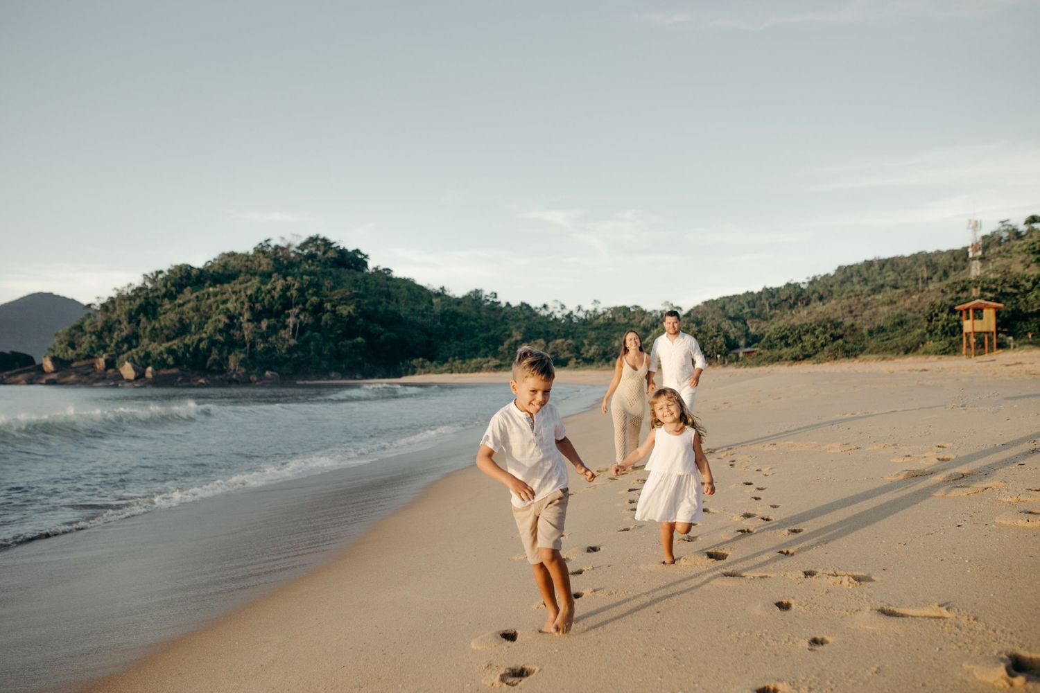 Family playing and running together on scenic beach at sunset.