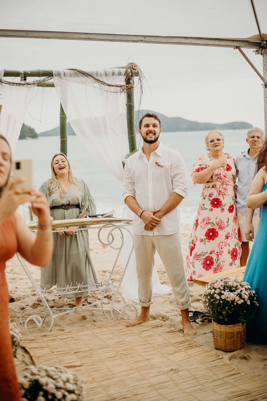 Guests gathering under a white canopy for a beach ceremony.