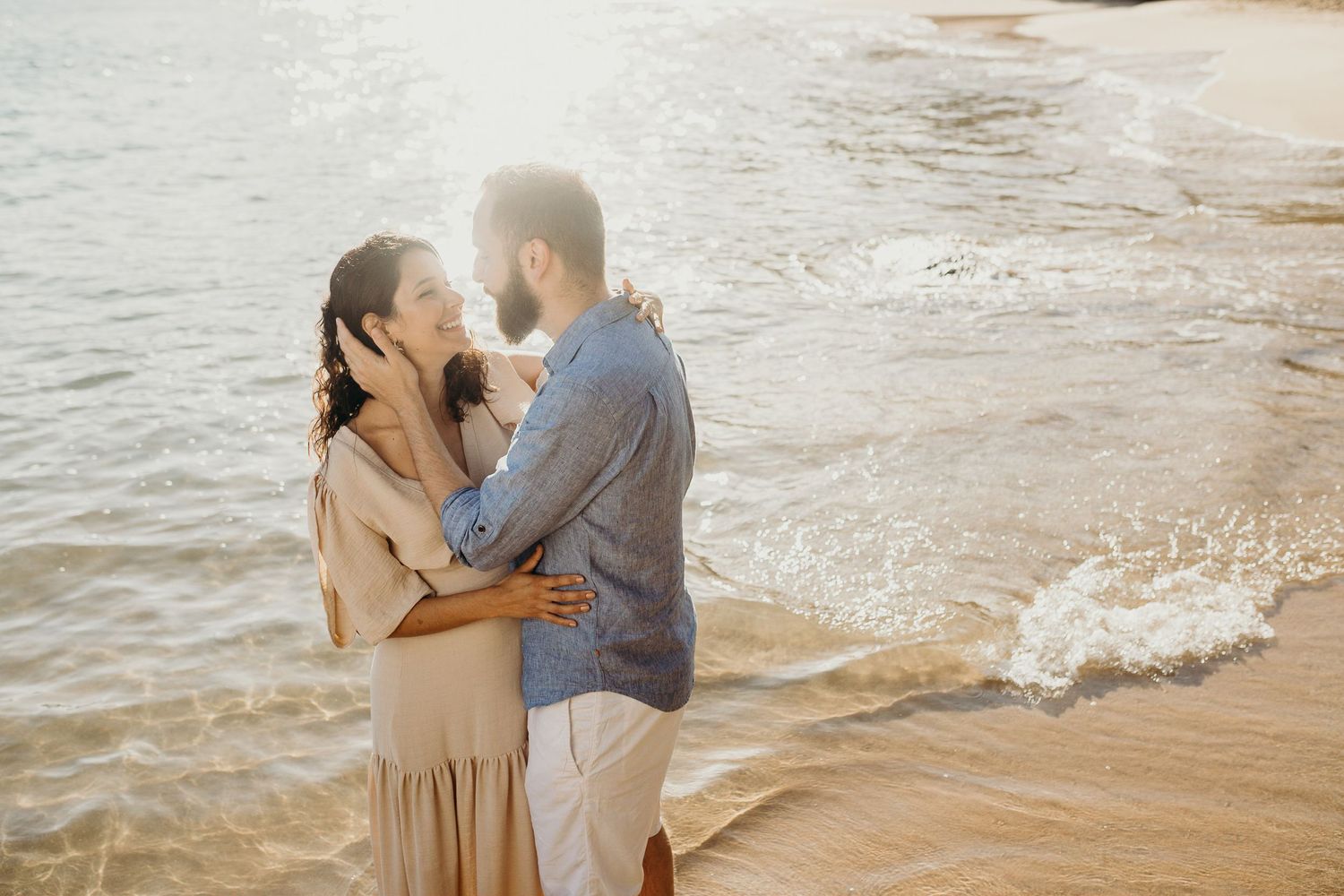 Couple sharing tender moment by ocean waves during sunset.