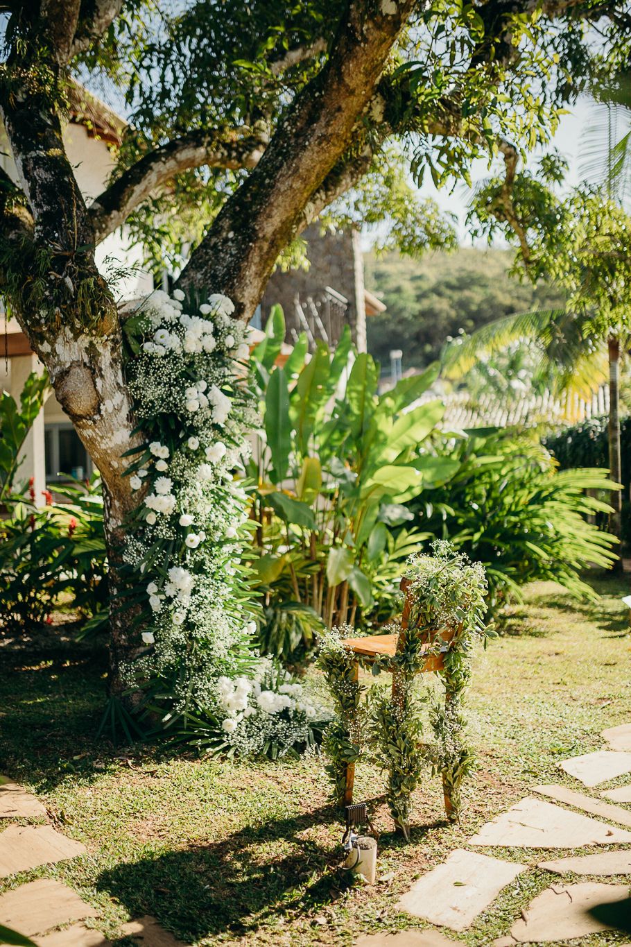 A garden pathway lined with white flowers and lush tropical plants under trees.