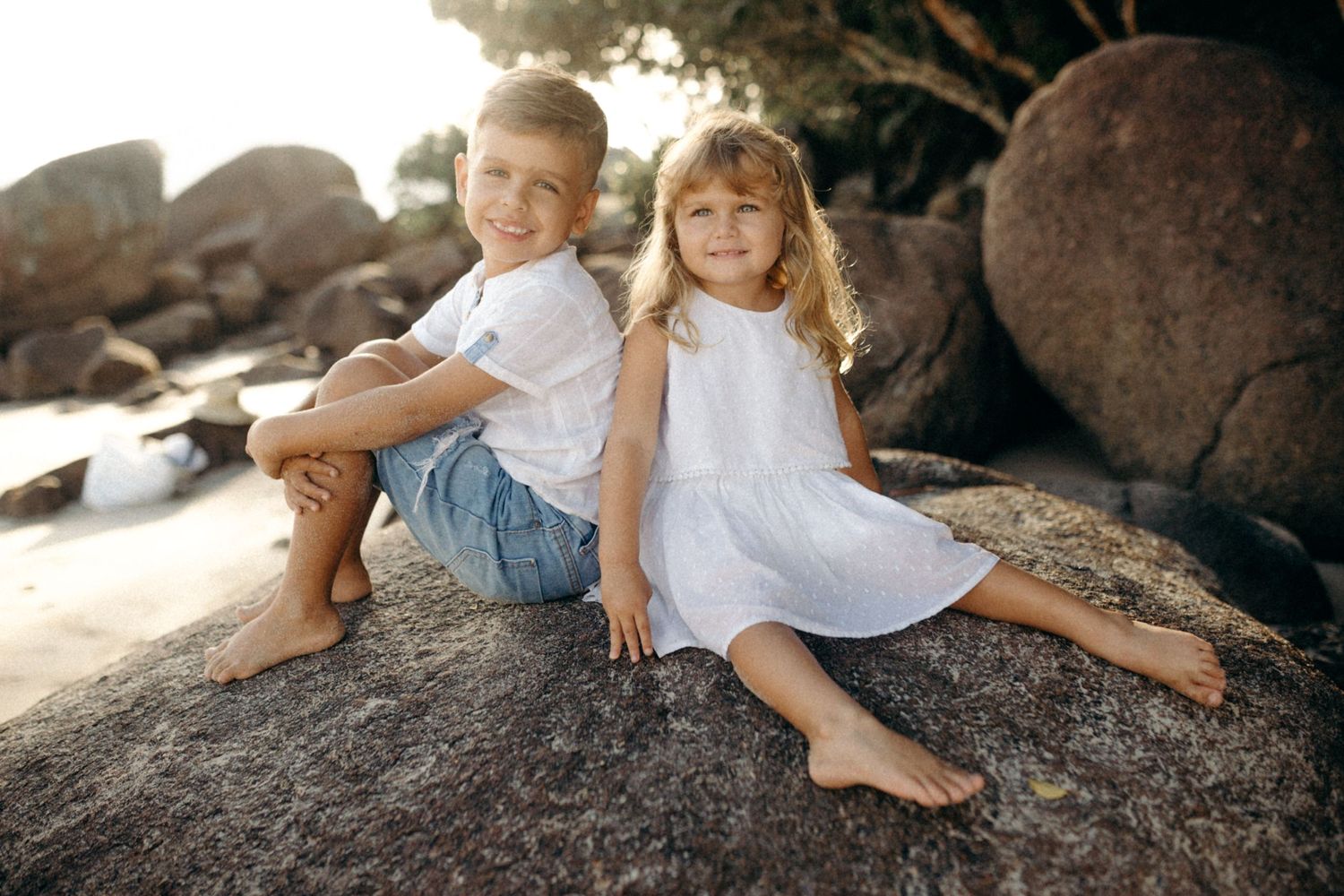 Children relaxing on large coastal rocks during beach photoshoot.