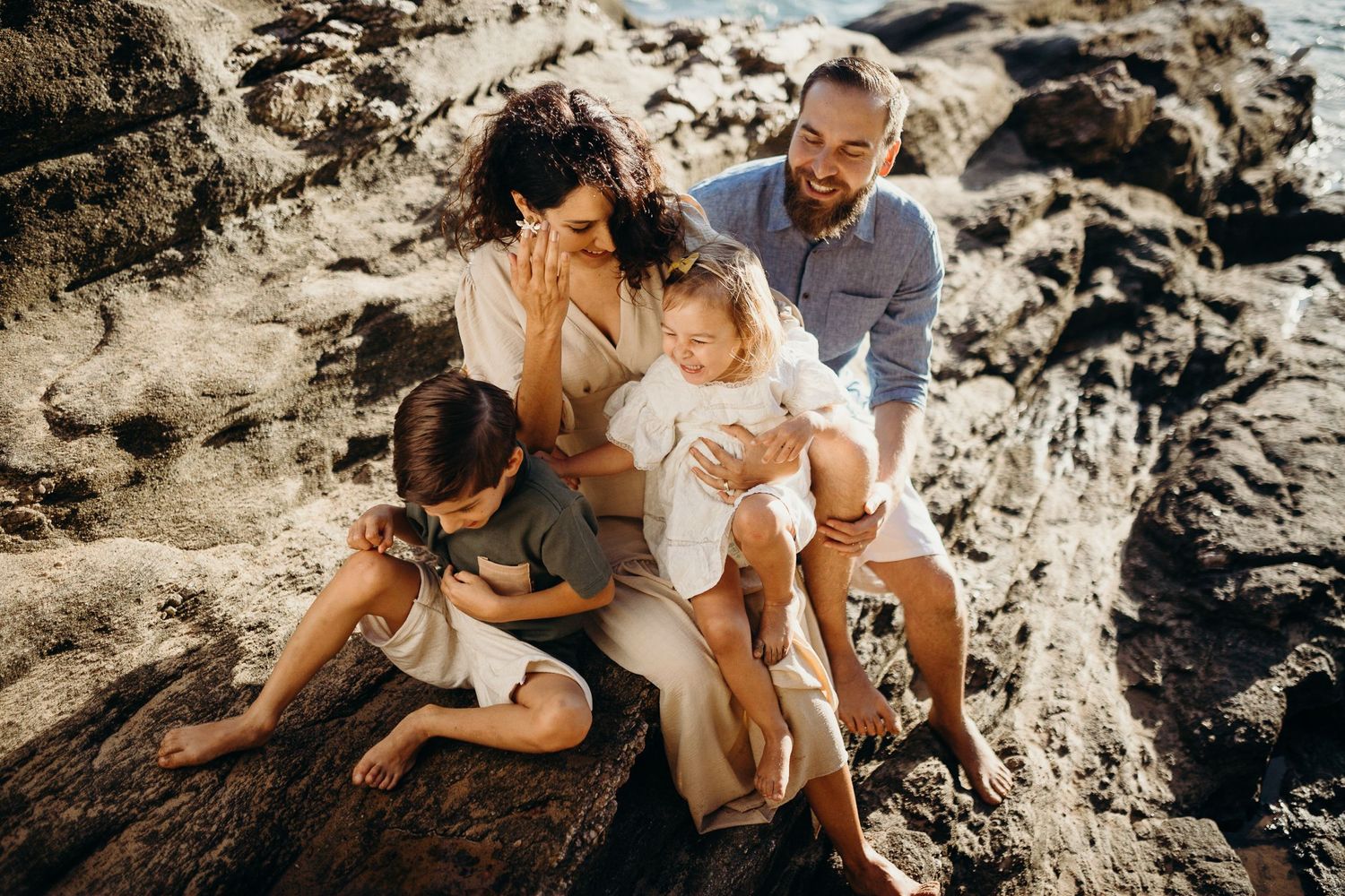 A candid family photo showing playful interaction while perched on rocky seaside cliffs.