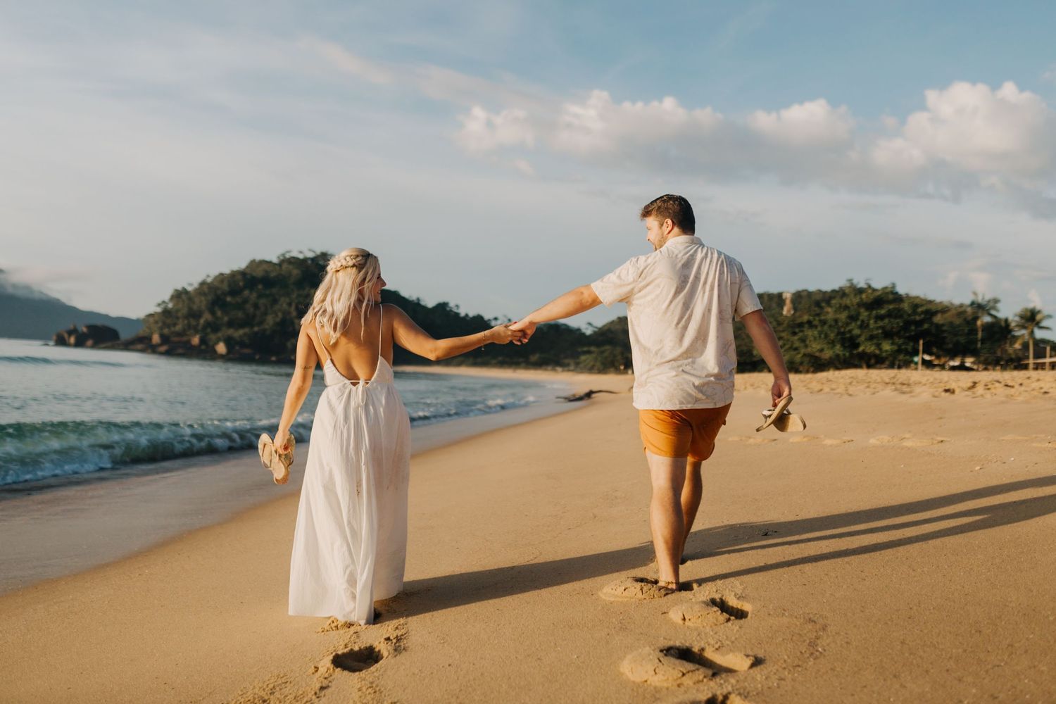 Romantic beach stroll with couple holding hands leaving footprints in golden sand.