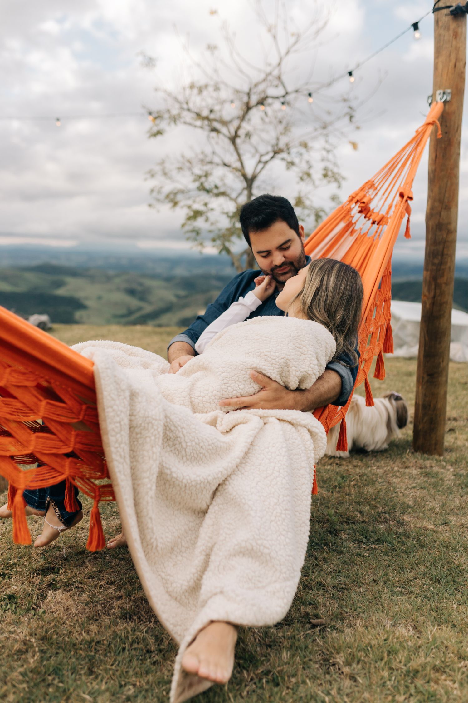 Romantic couple relaxing in an orange hammock with mountain views and a cozy blanket.