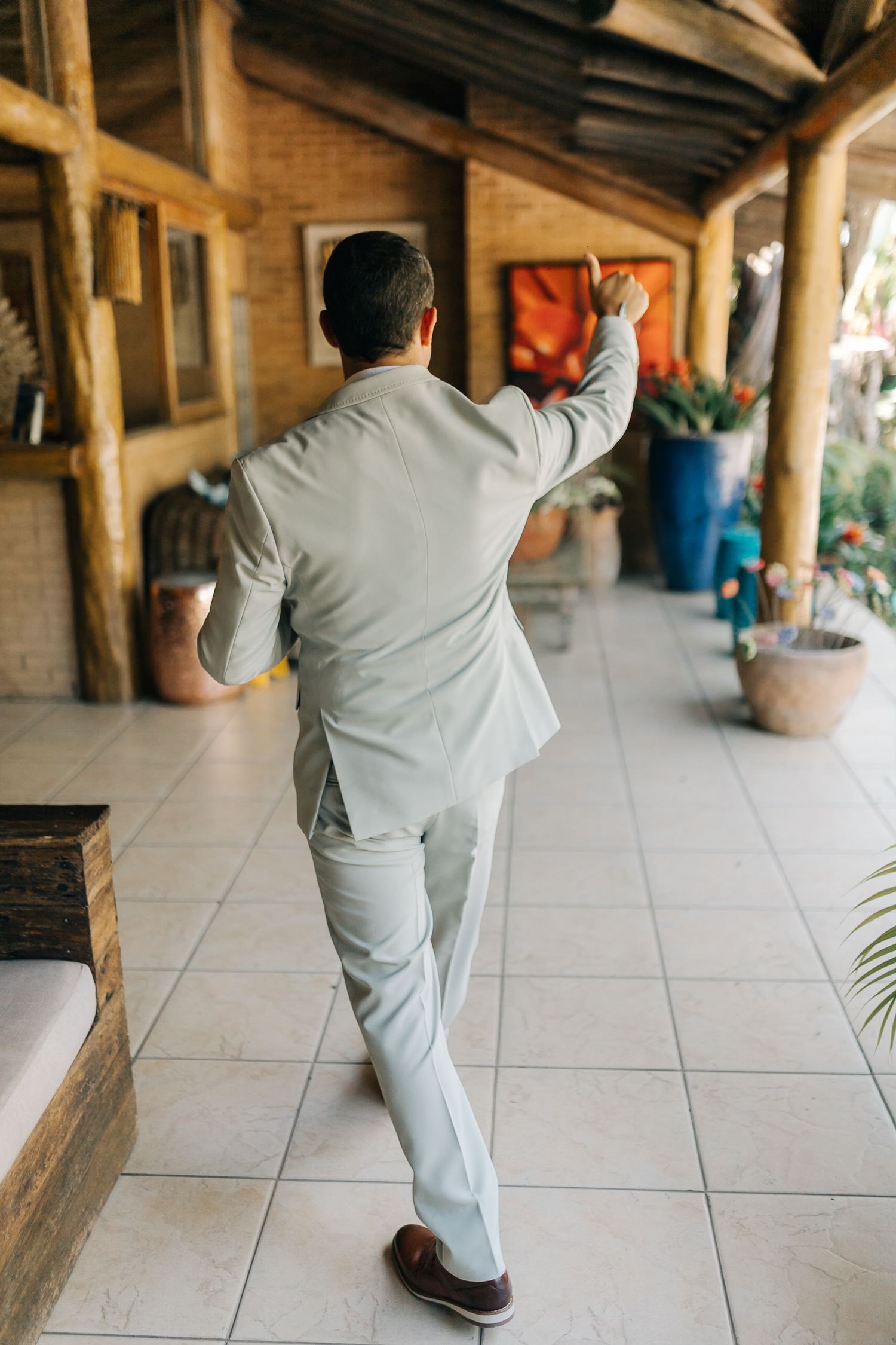 Person in light grey suit walking down tiled hallway viewed from behind.