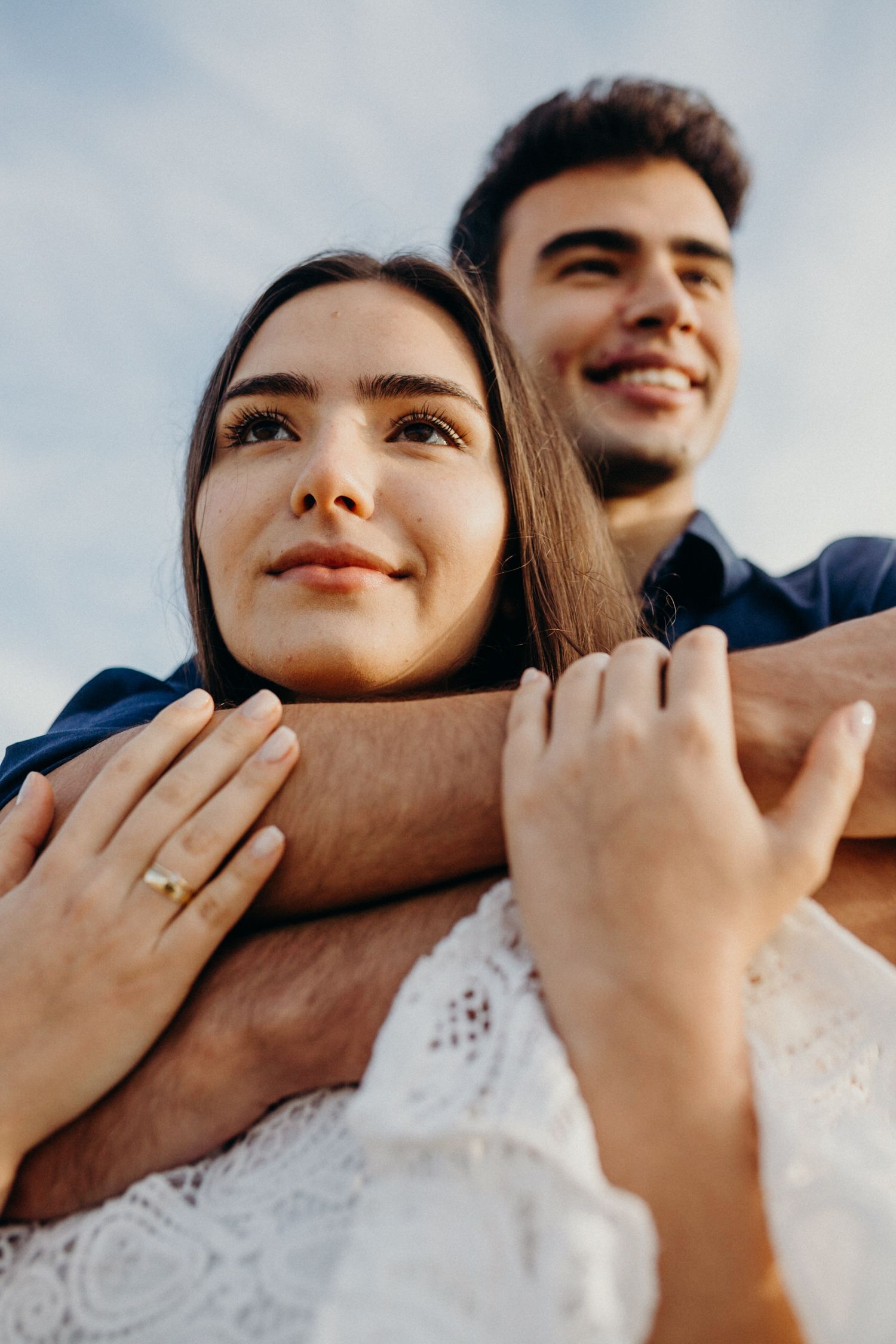 Close-up shot of a couple embracing with soft natural lighting and a visible engagement ring.