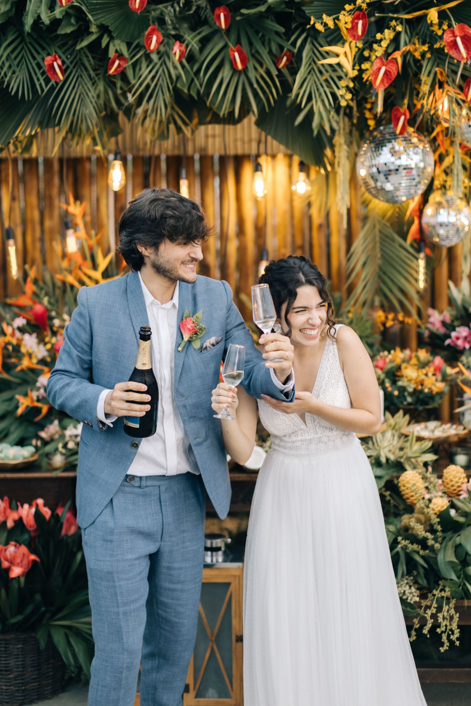 Newlyweds toasting with drinks at tropical-themed wedding reception.