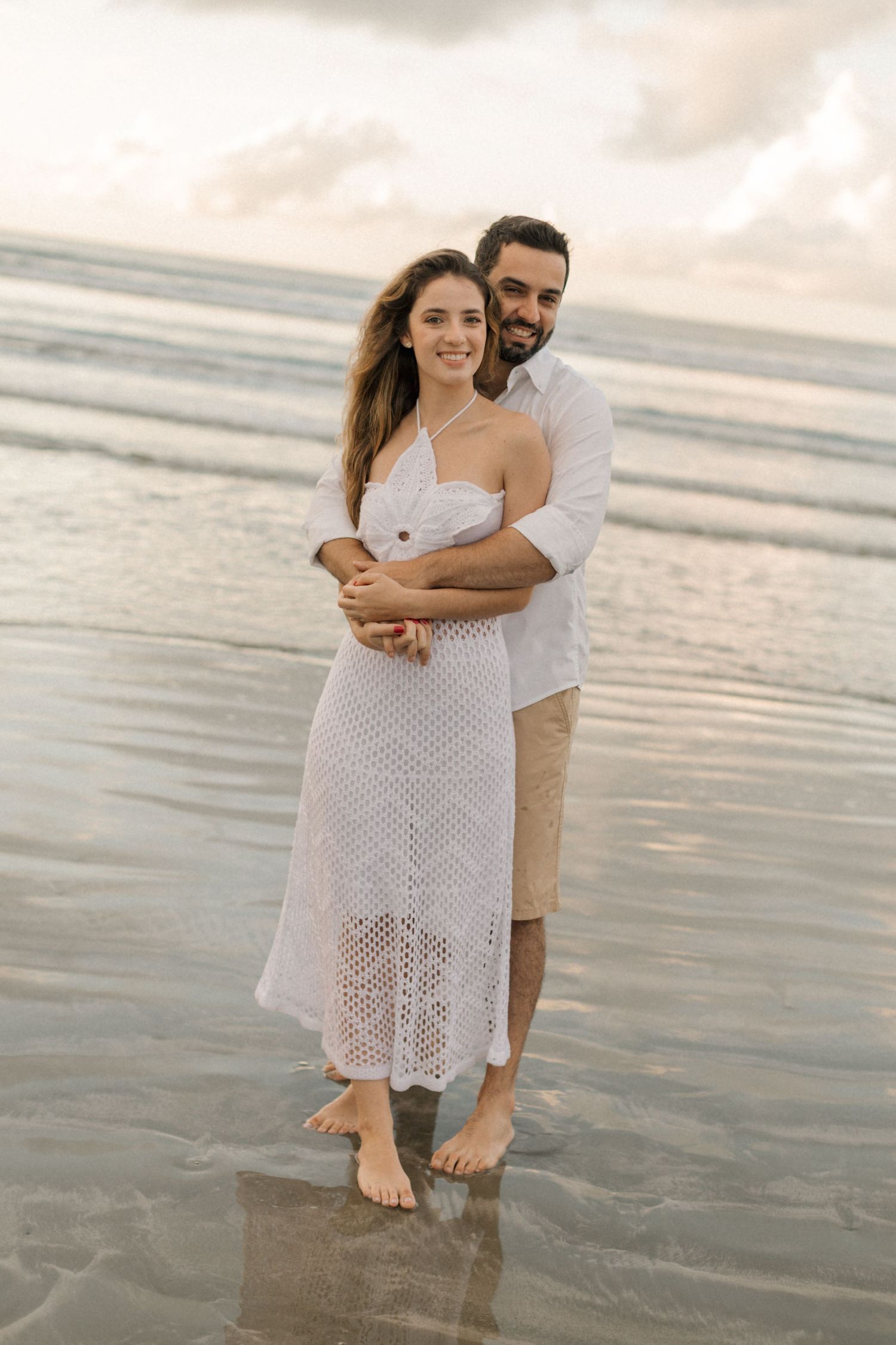 Romantic beachside portrait of couple embracing on wet sand during golden hour.