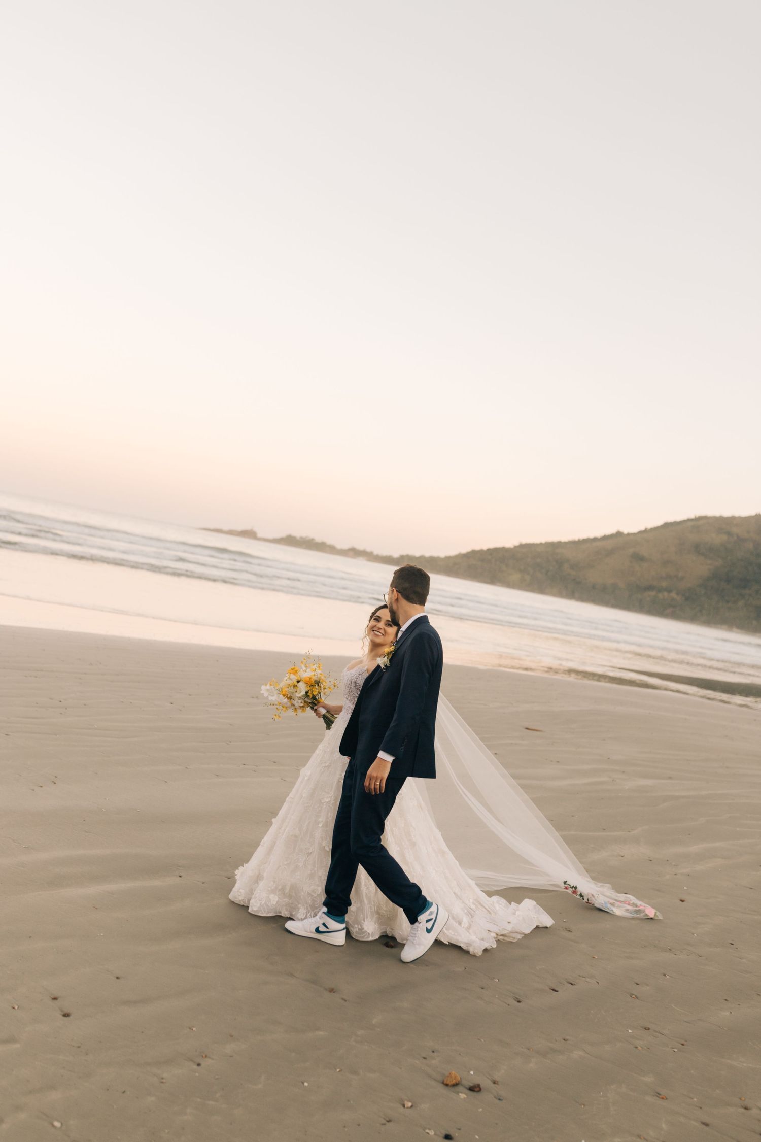 Romantic beach wedding portrait with couple walking along shoreline at sunset.