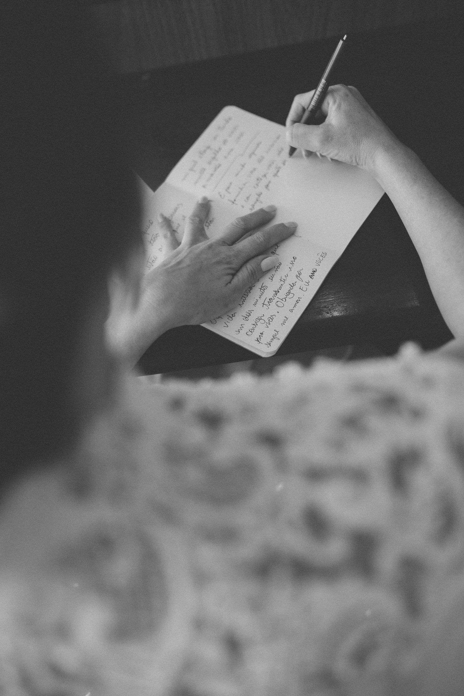 Hands writing in a notebook shown in moody black and white photography.