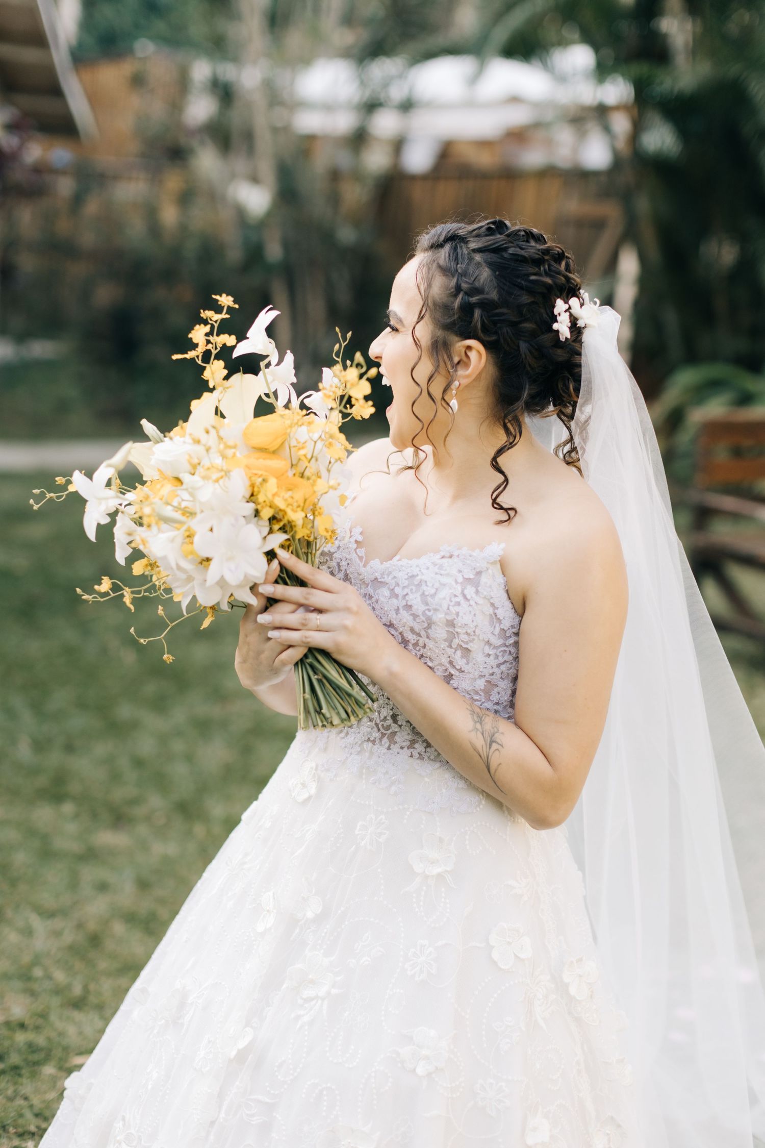A stunning white wedding dress with an elegant yellow and white bouquet in an outdoor garden setting.