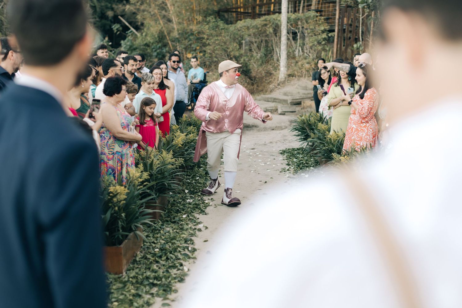 Guest walking down garden path at outdoor wedding while others watch from sides.