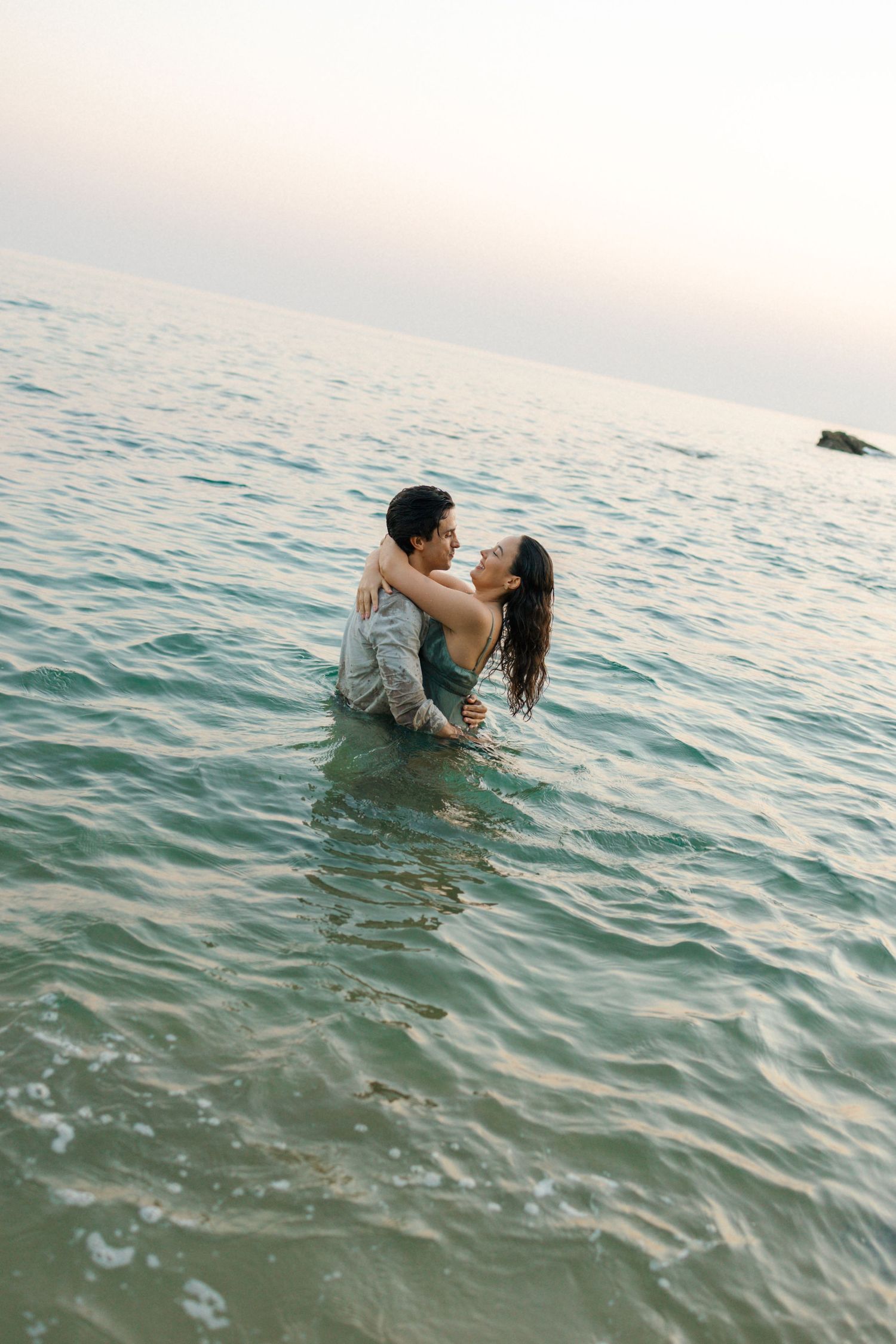 A pair share an intimate moment while floating together in turquoise ocean waters on a bright day.