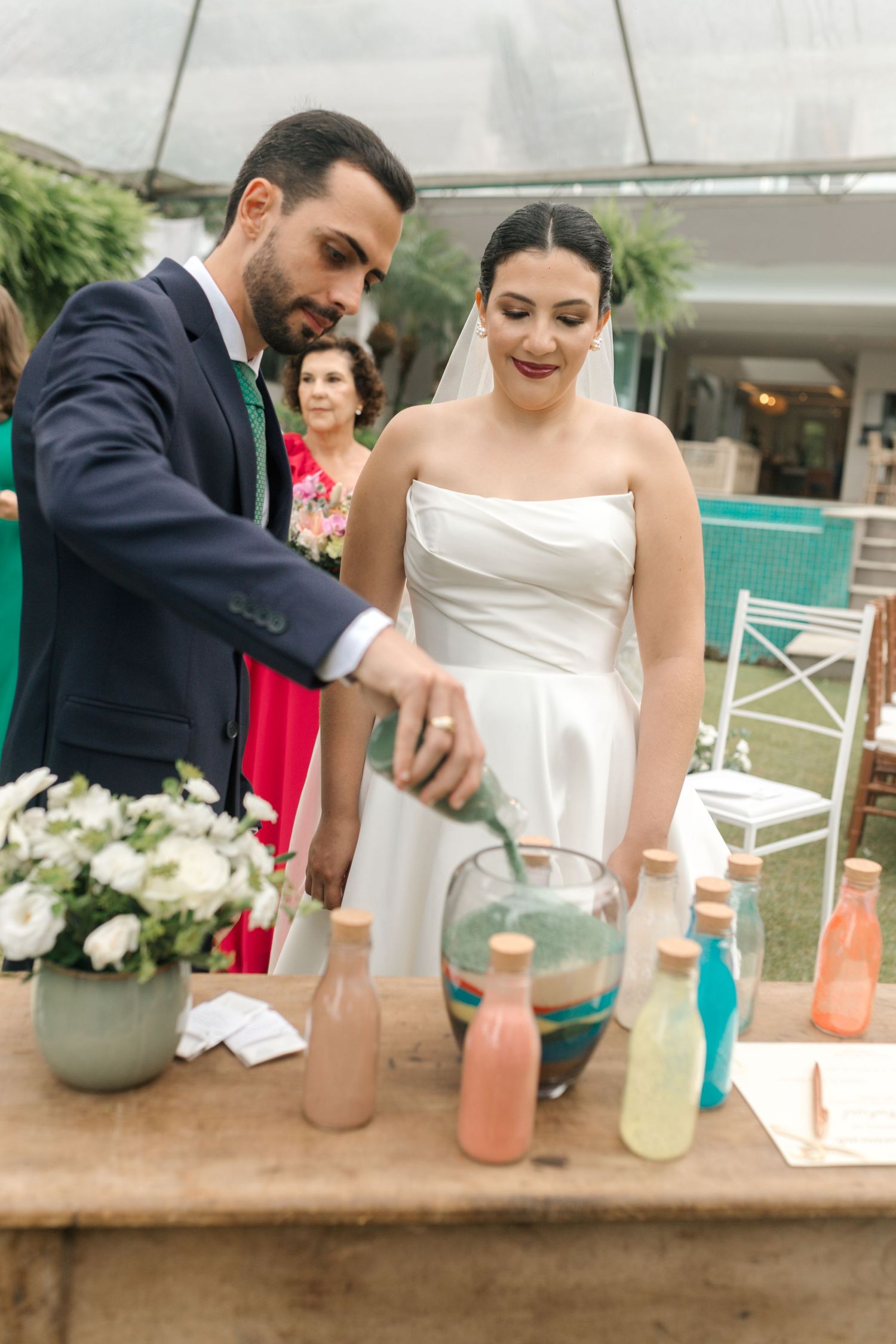 Wedding couple pouring colorful drinks at rustic beverage station during outdoor reception.