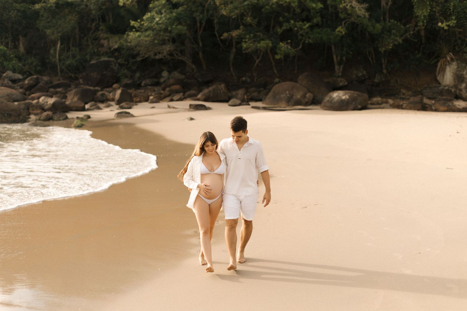 Couple walking hand in hand along a tranquil beach at sunset.