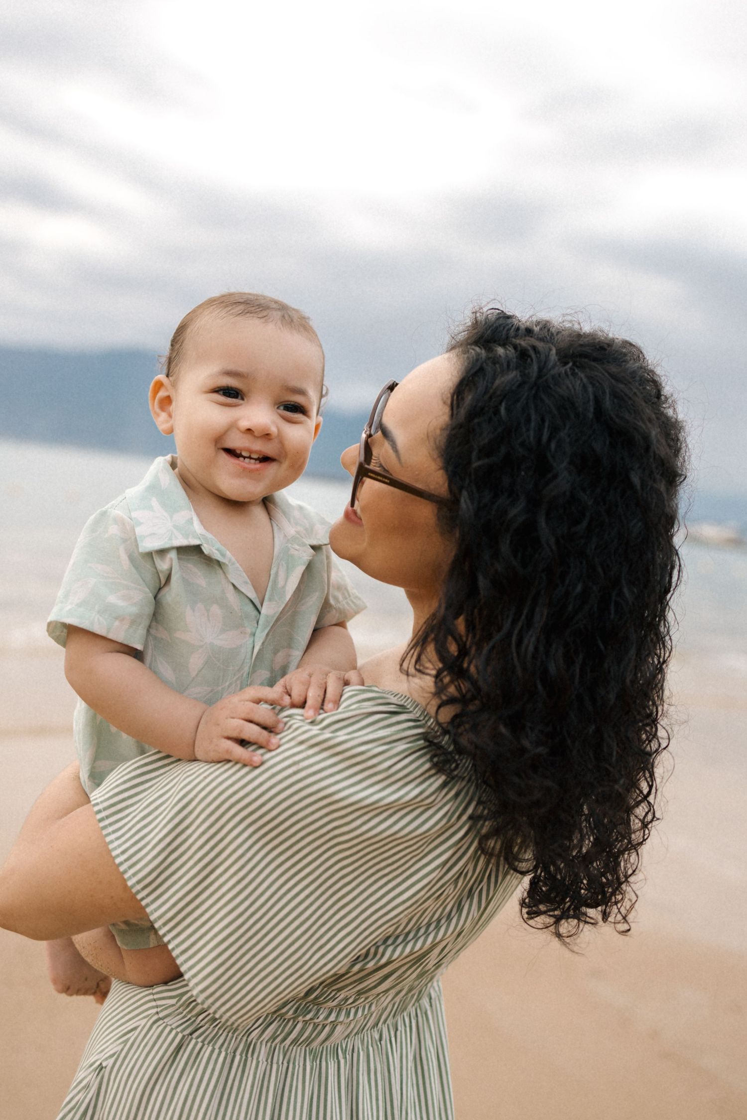 A tender moment of connection and laughter shared between parent and baby against a cloudy sky backdrop.