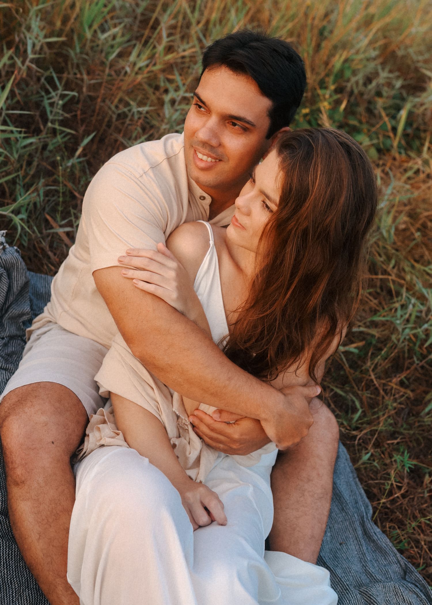 Happy couple embracing on blanket during outdoor photoshoot in nature.