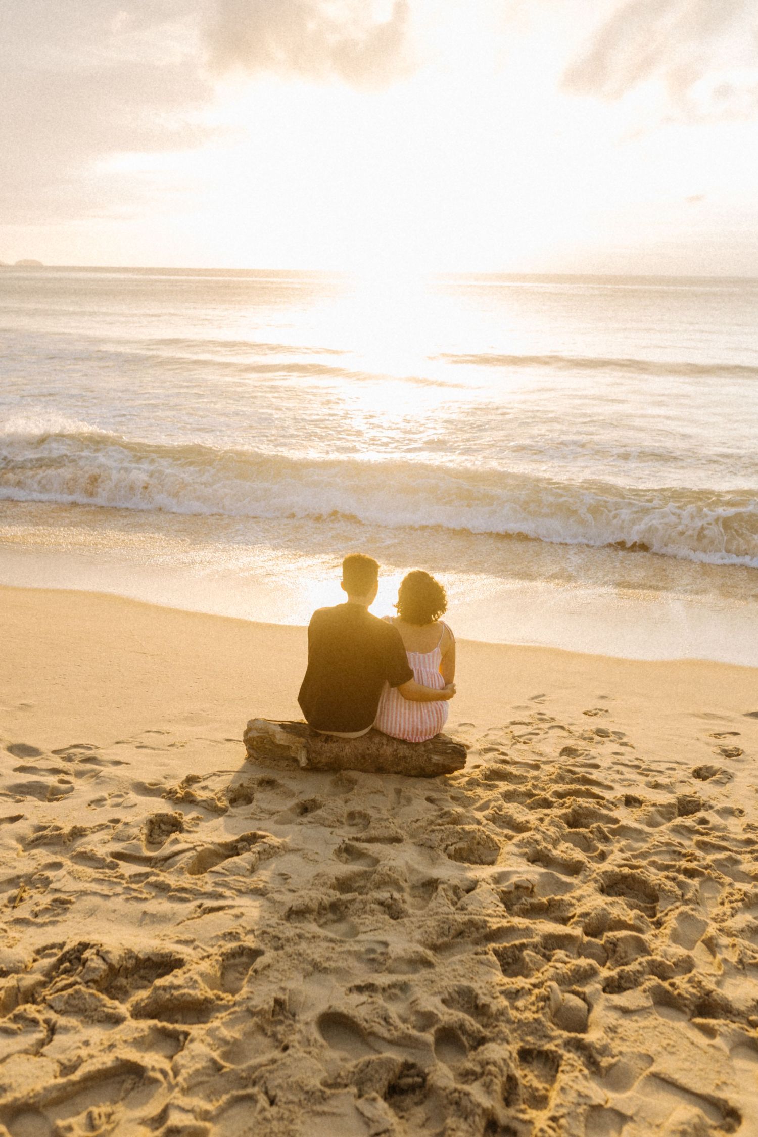 Casal sentado na praia assistindo o pôr do sol sobre as ondas do mar durante a hora dourada.