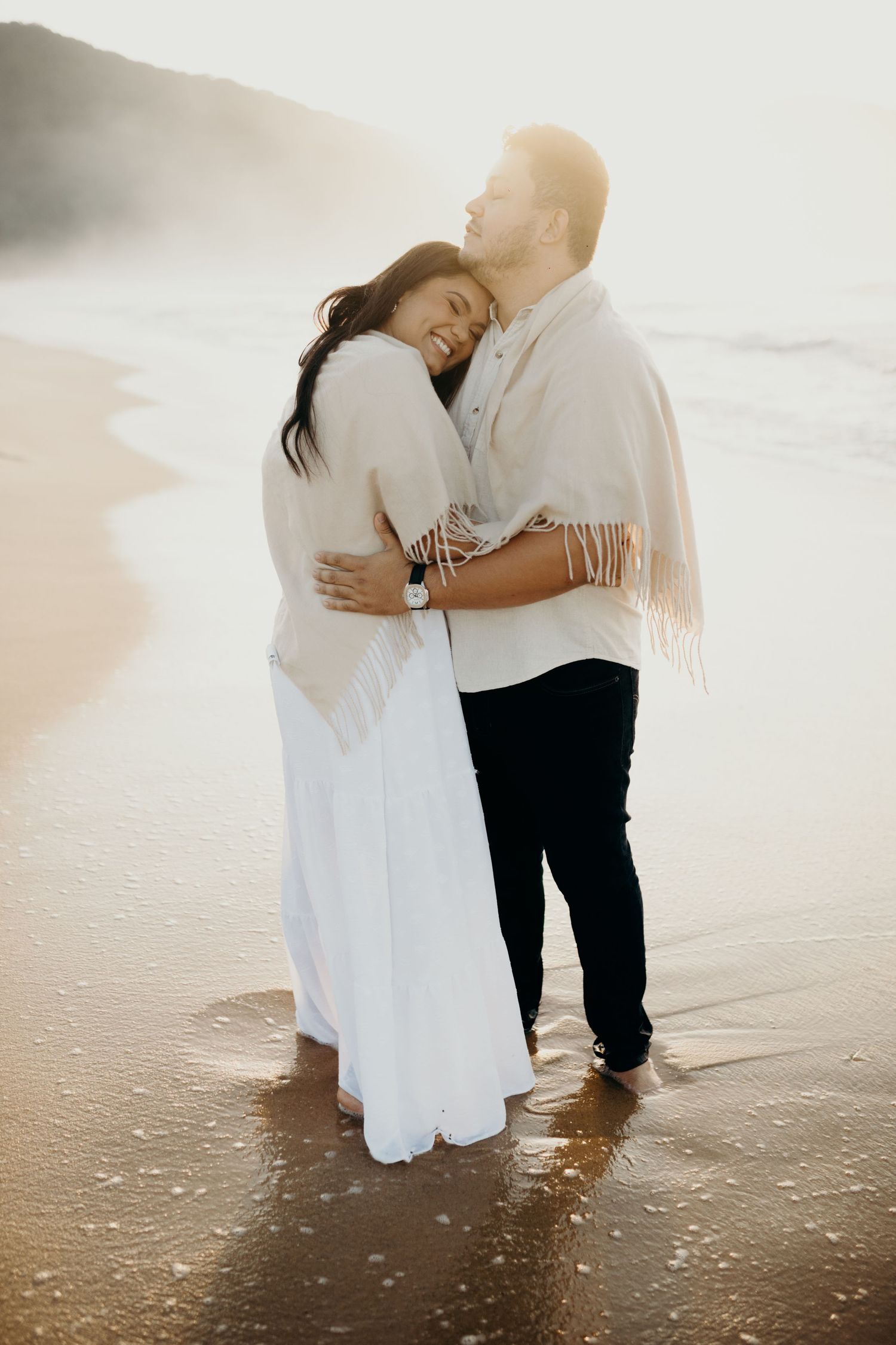 Couple standing in shallow ocean water wearing white and black outfits during a beach photoshoot.