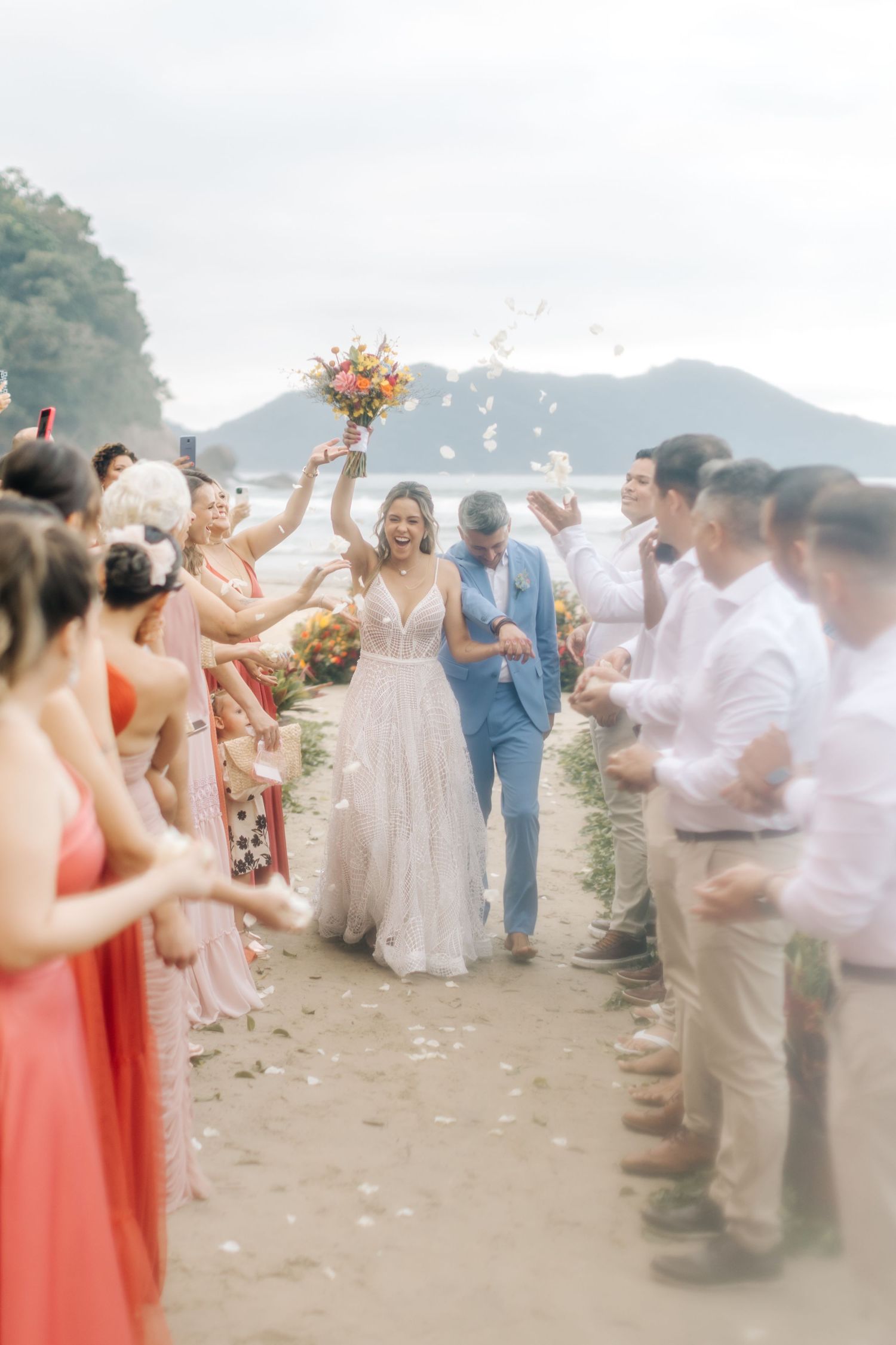 Wedding guests throwing petals and celebrating on a misty beach with mountains in the background.