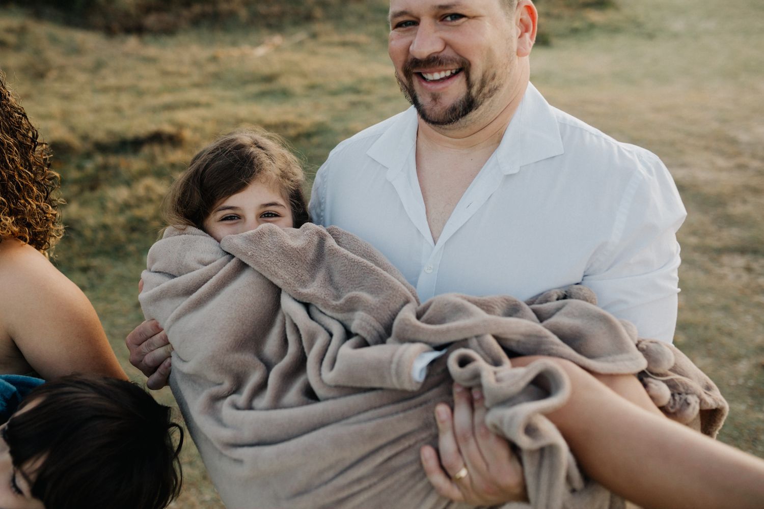 A heartwarming family moment captured outdoors with gentle smiles and a grey blanket.
