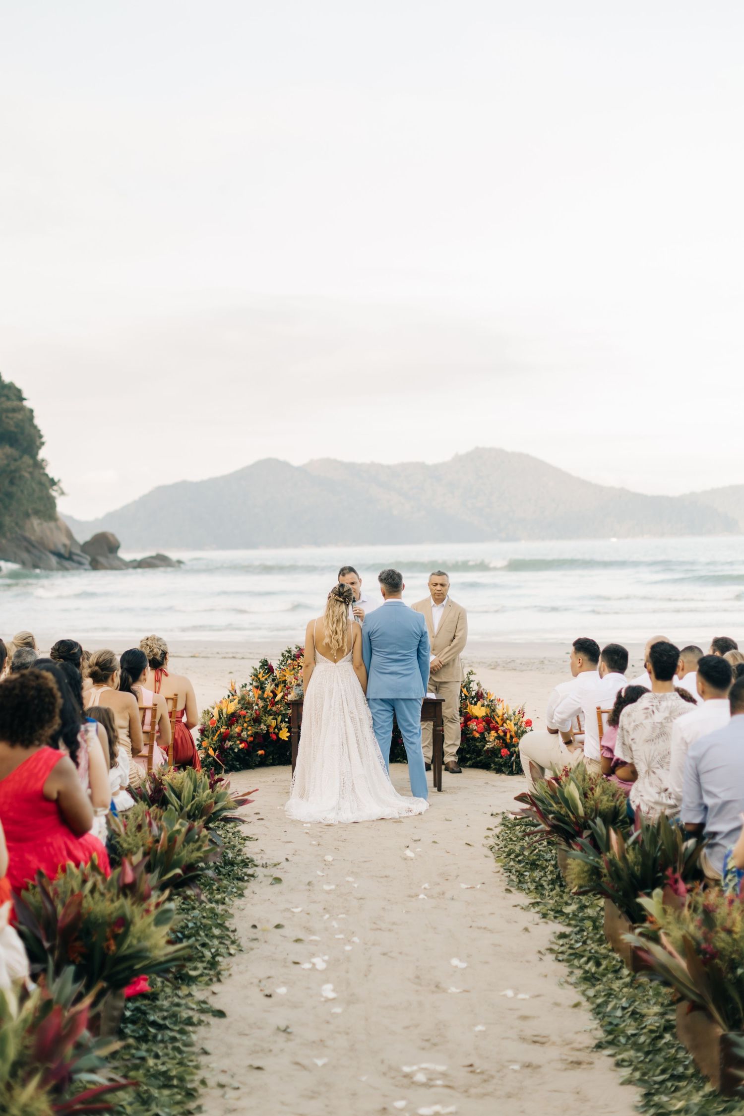 Scenic beach wedding ceremony with floral aisle decorations and mountain views.