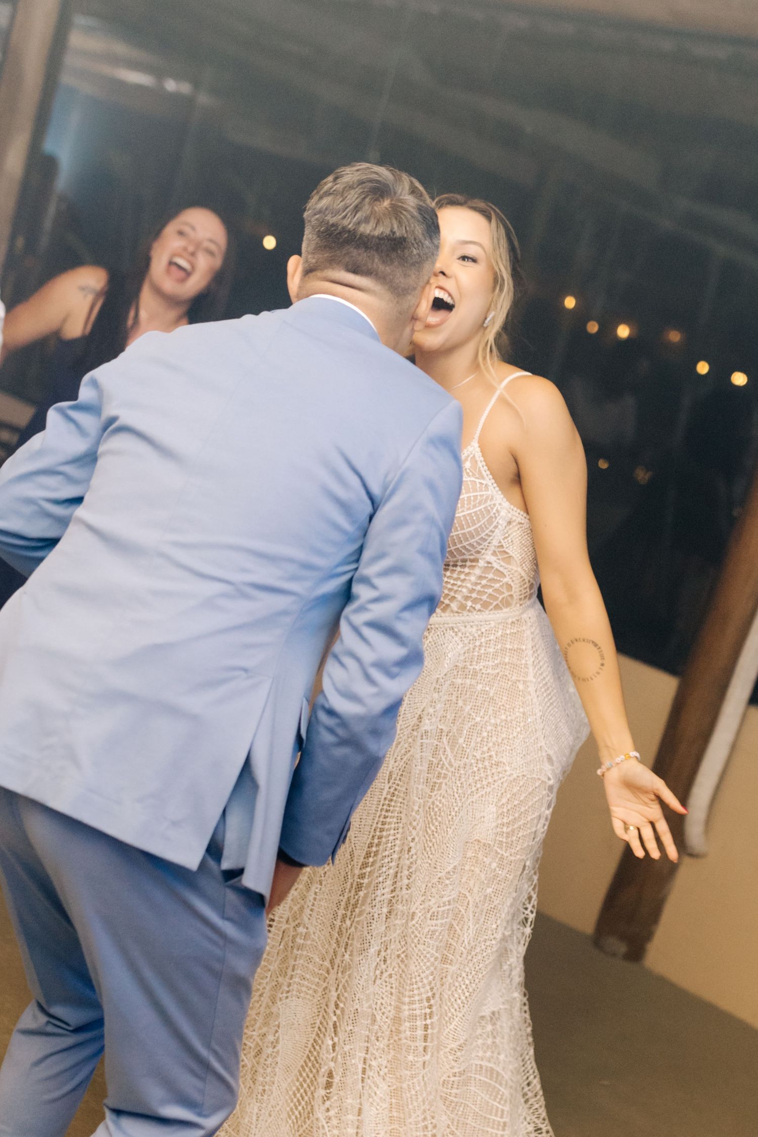 Joyful dance celebration at wedding reception with lace dress and blue suit in motion.