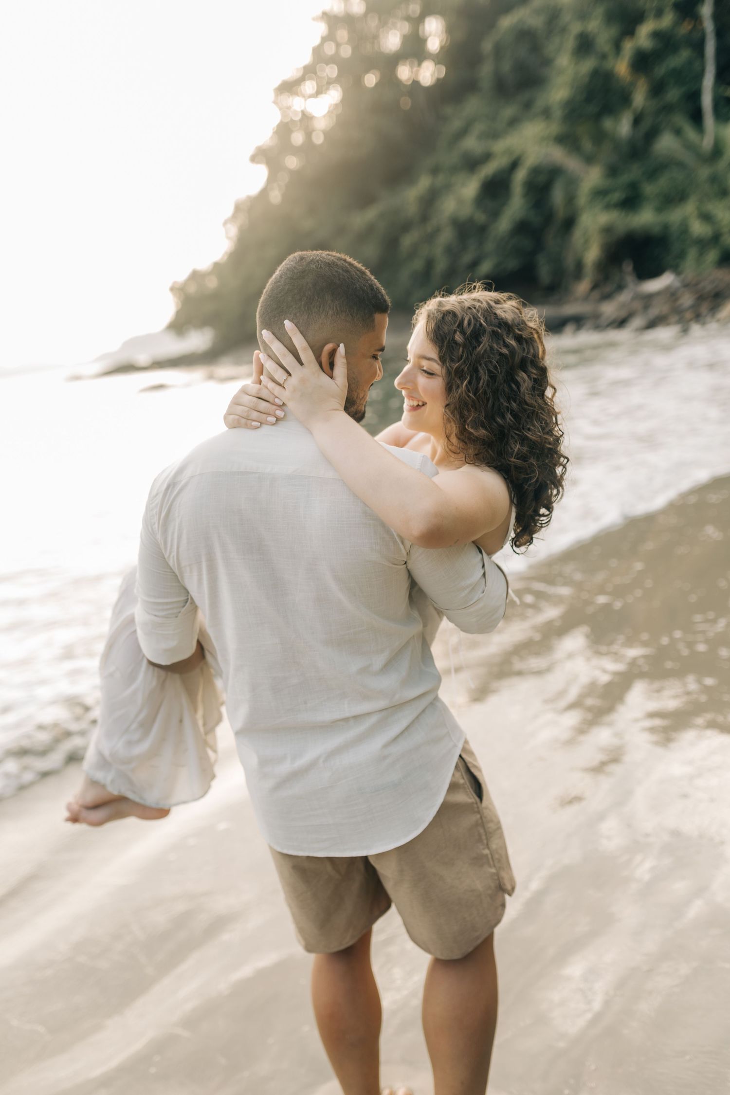 A couple embraces on a sandy beach during golden hour with scenic coastal views.
