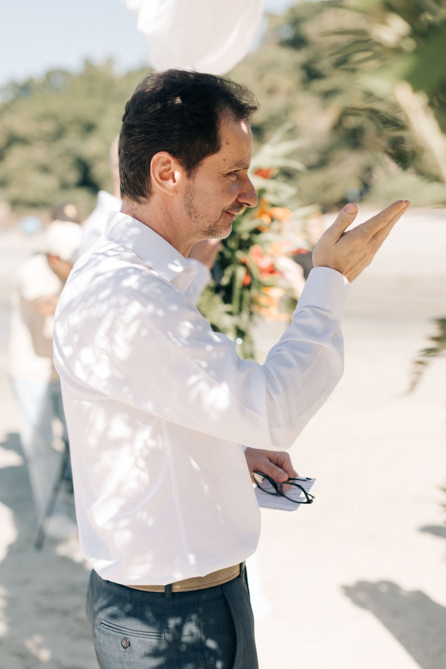 Wedding officiant gestures while speaking during outdoor ceremony.