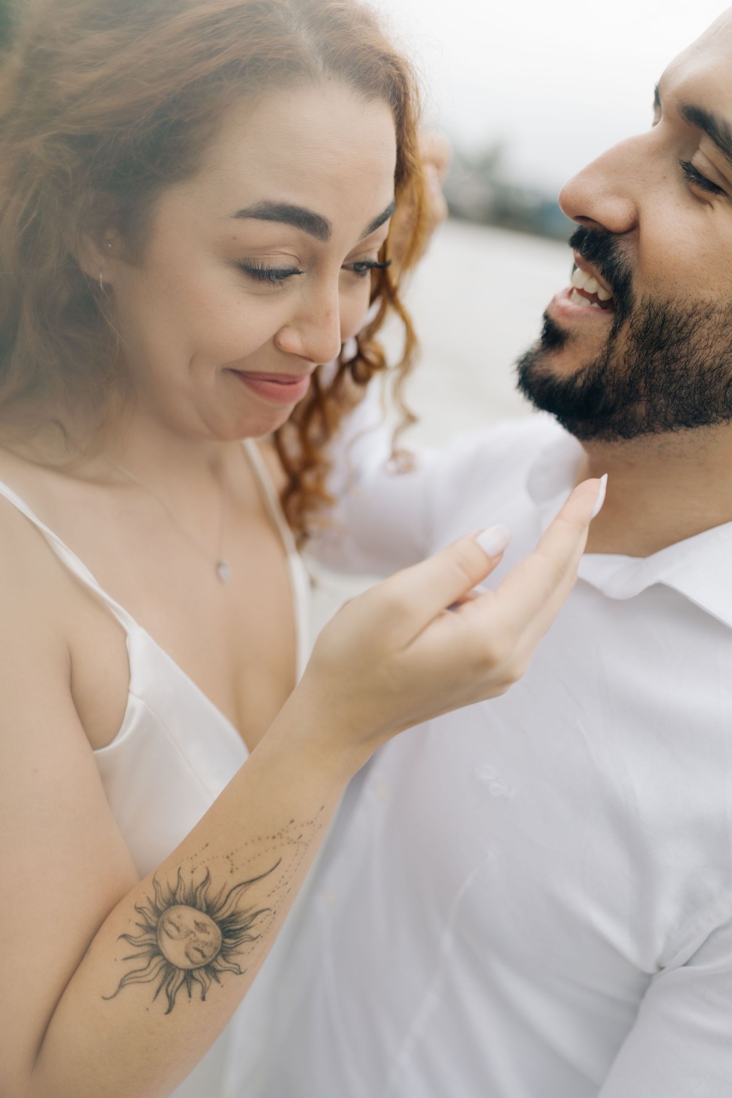 Close-up beach portraits showing tender moments with visible sun and flower tattoos.