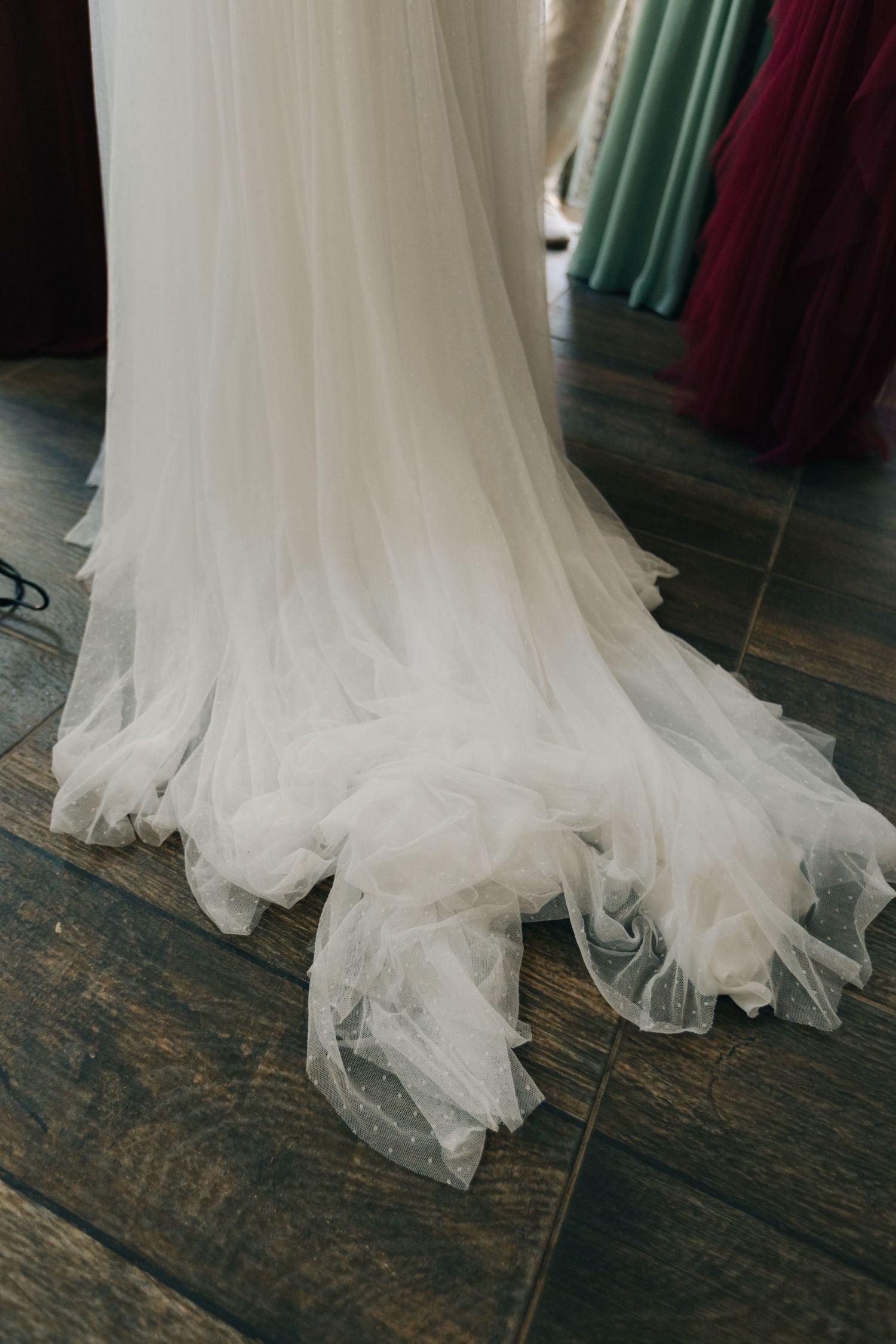 Close-up of a flowing white wedding dress train on dark wooden flooring.