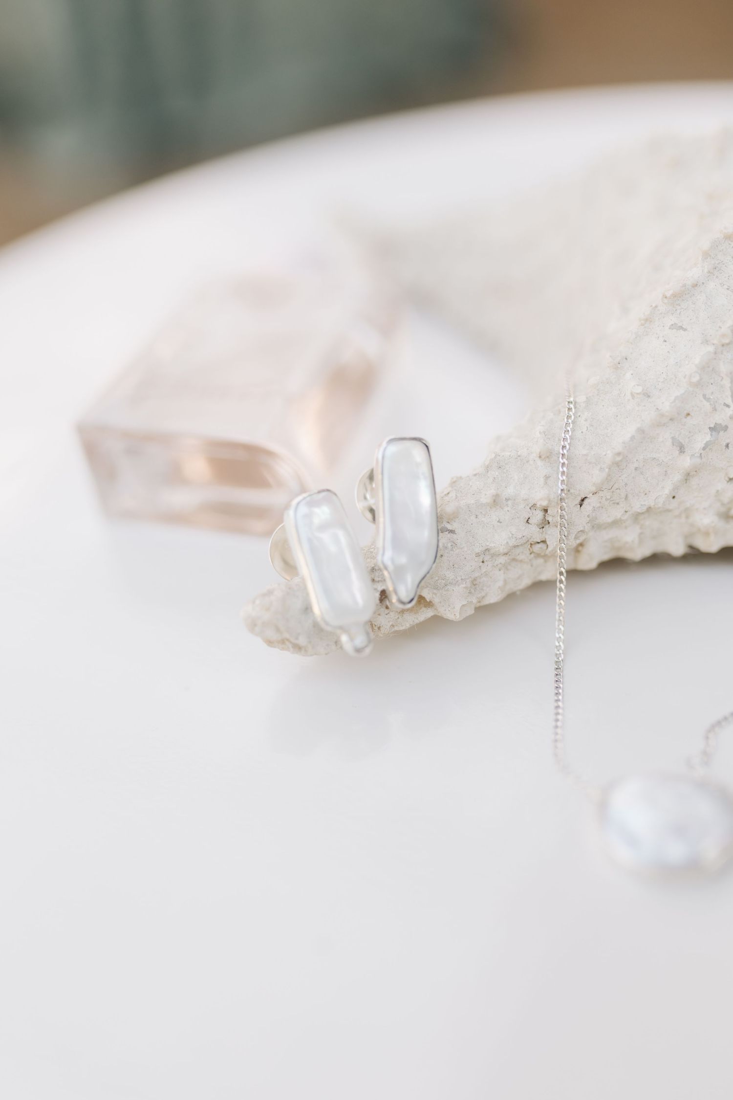 Delicate pearl earrings and jewelry displayed on white lace fabric in soft lighting.