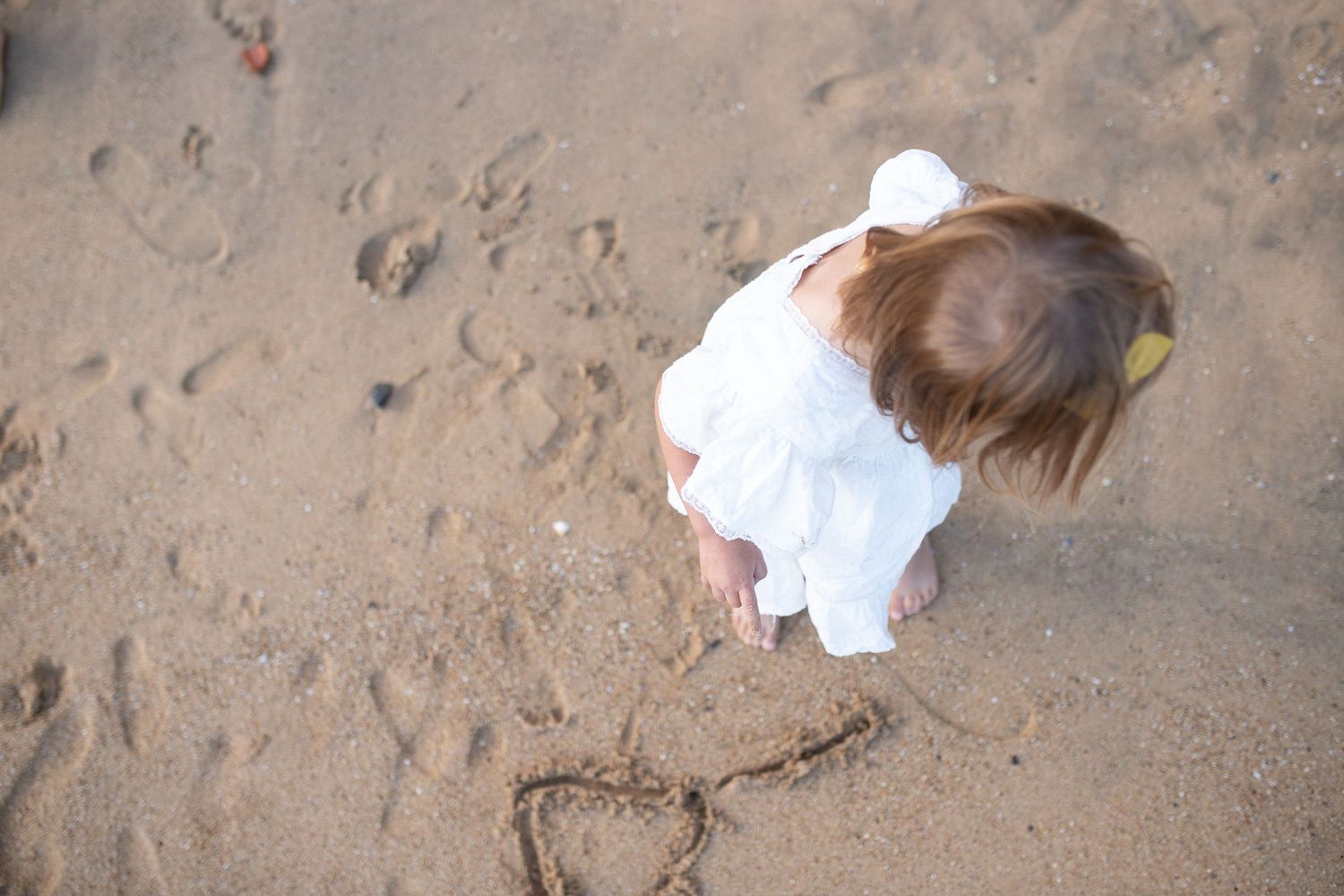 An aerial view of a heart drawn in beach sand with someone wearing white looking down.