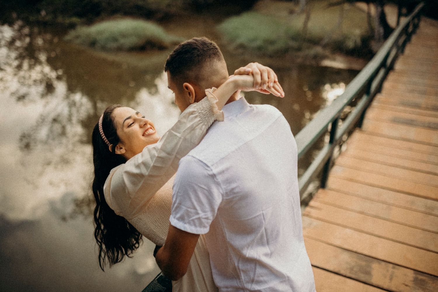 Couple sharing an intimate moment while dancing on a wooden bridge outdoors.