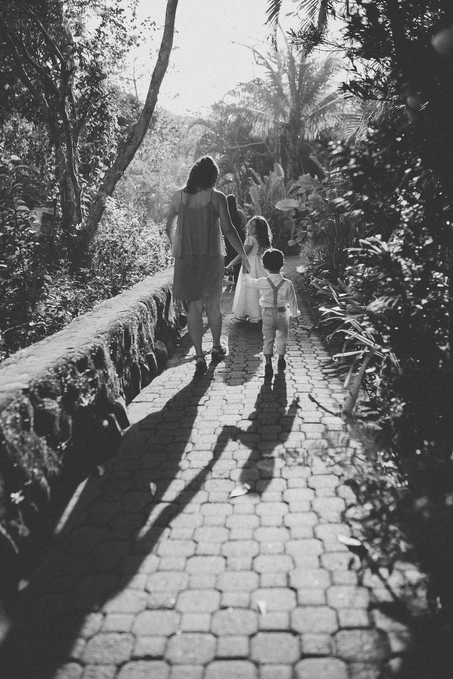 Black and white silhouette of people walking along a garden path surrounded by trees.