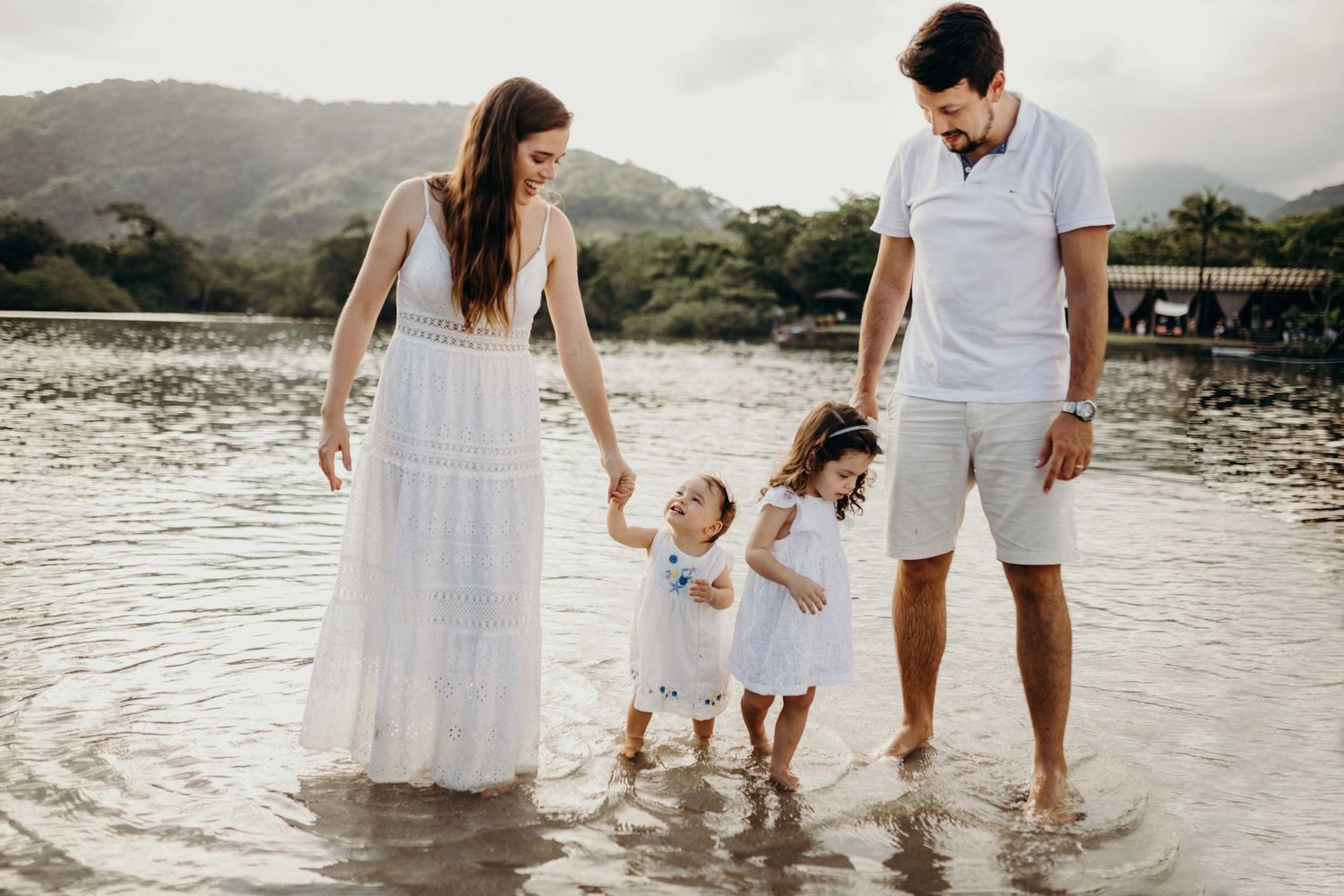 A family wearing white outfits plays together at the beach during sunset.