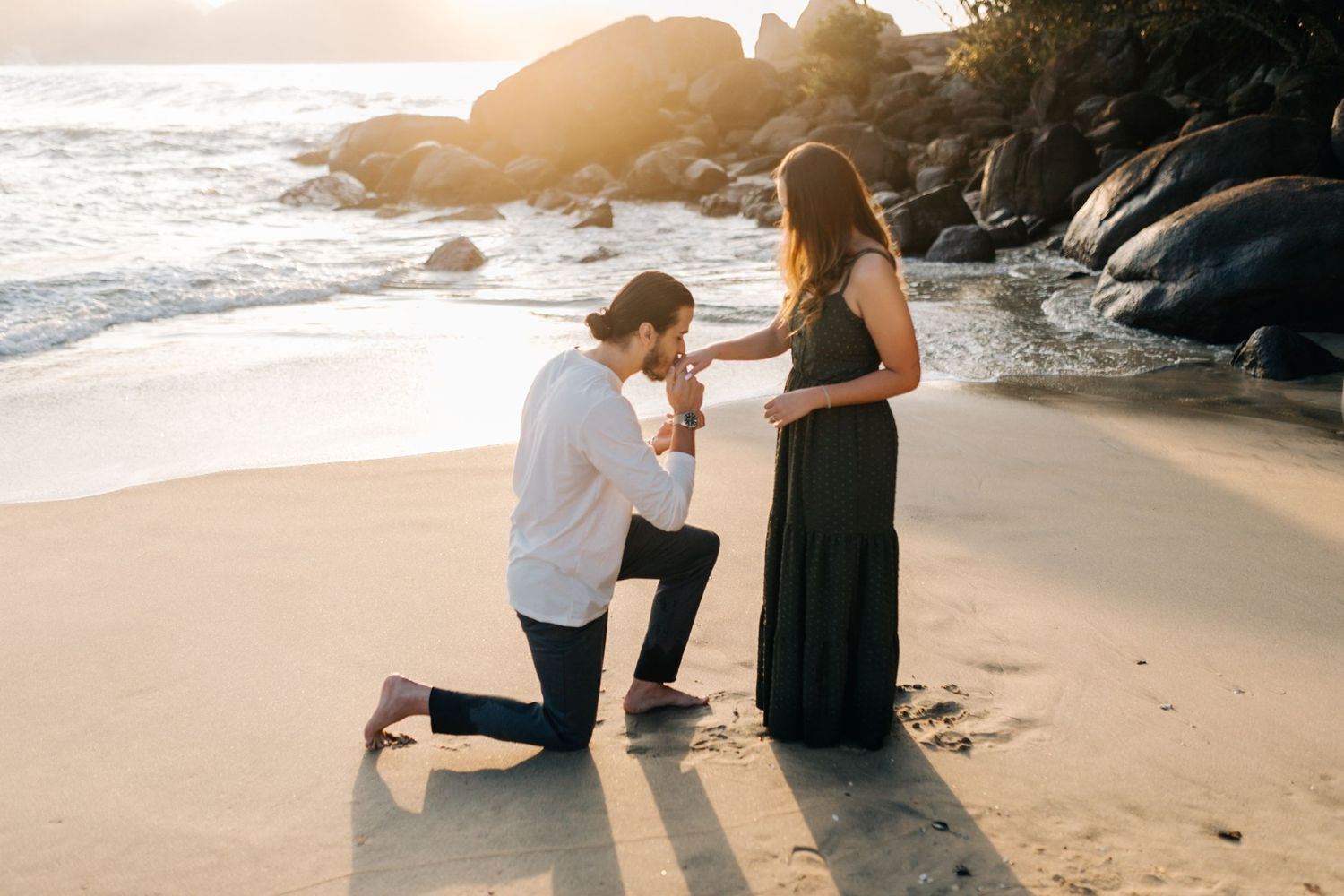A beautiful beachside proposal moment with mountains and ocean waves in the background.