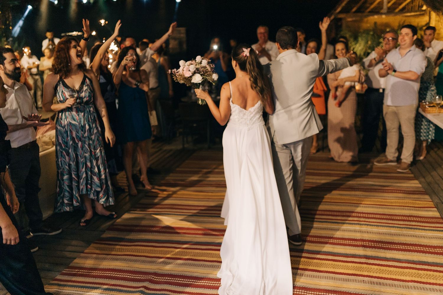 Wedding couple dances with guests celebrating on a colorful striped dance floor at their reception.