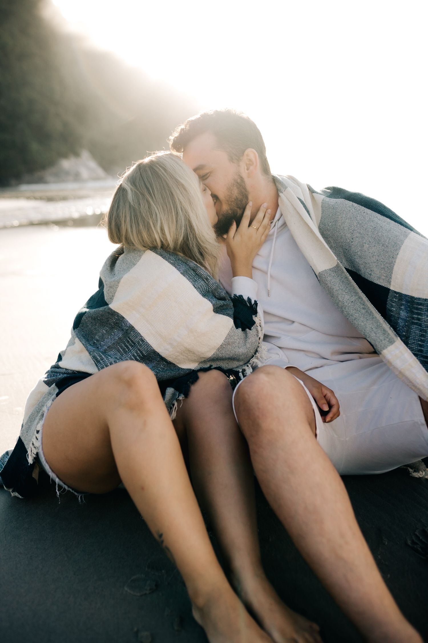Romantic beachside embrace captured during golden hour with coastal backdrop.