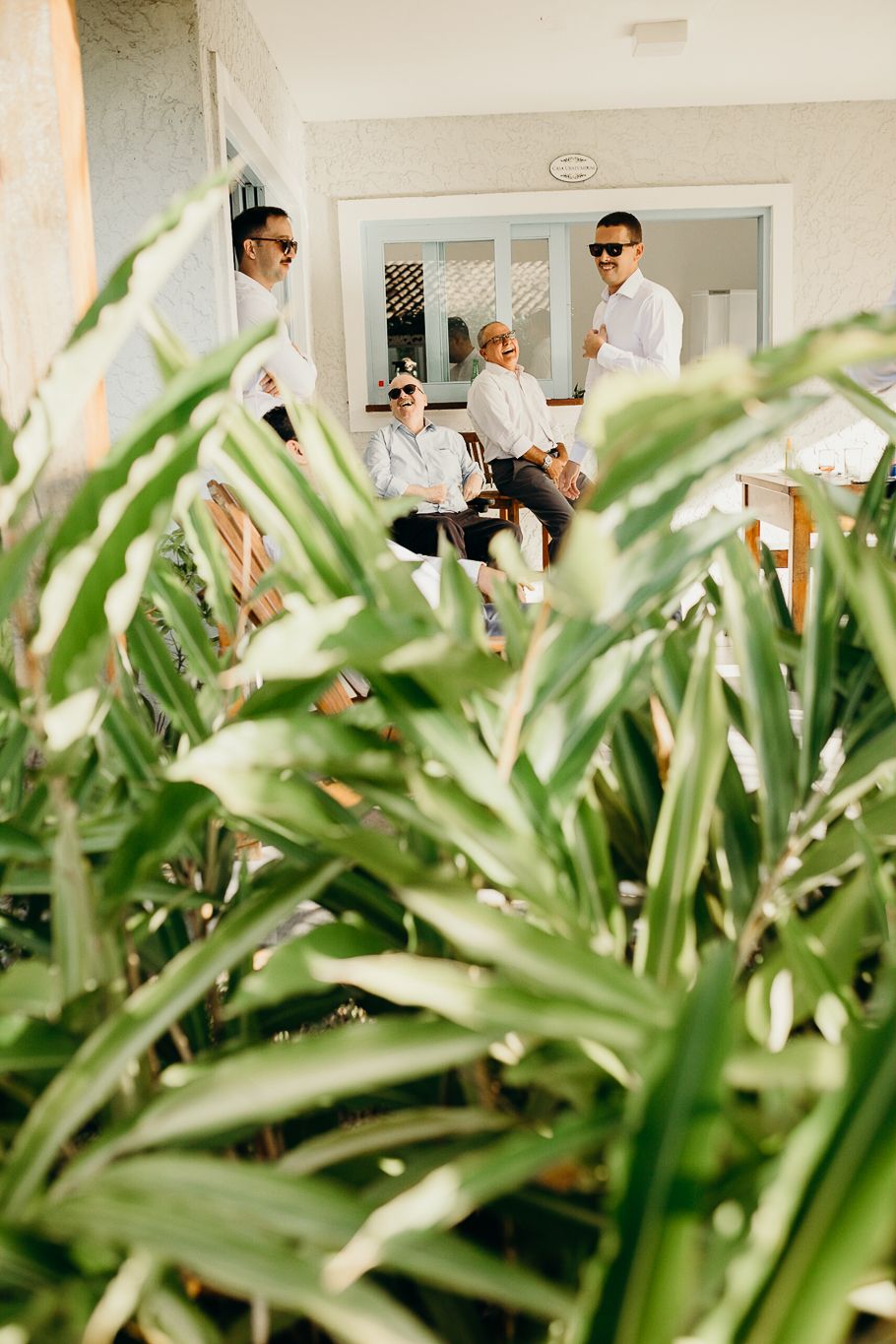 Lush tropical plants frame a white building entrance with casual outdoor seating.