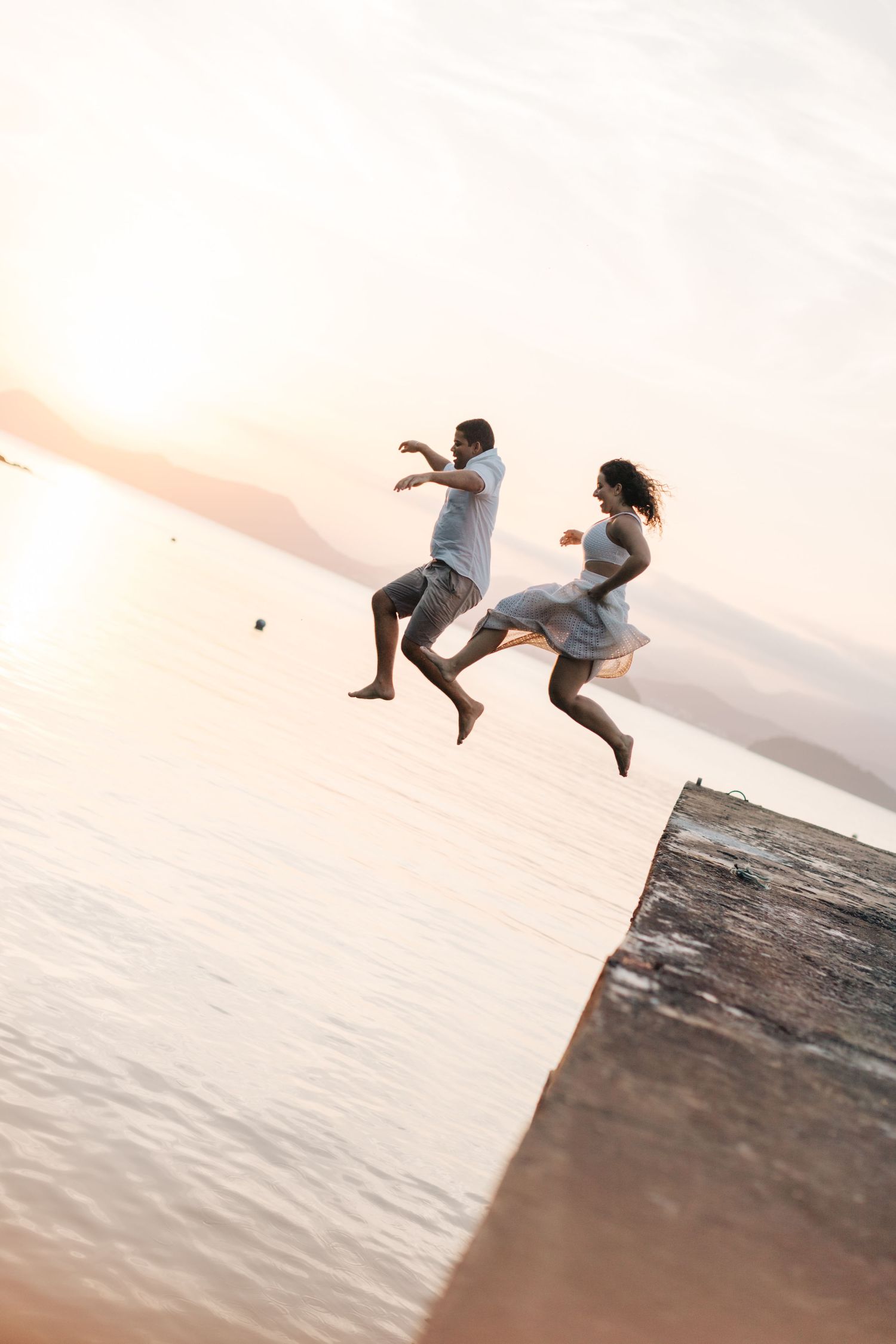 Two people jump off a pier into the water during golden hour.