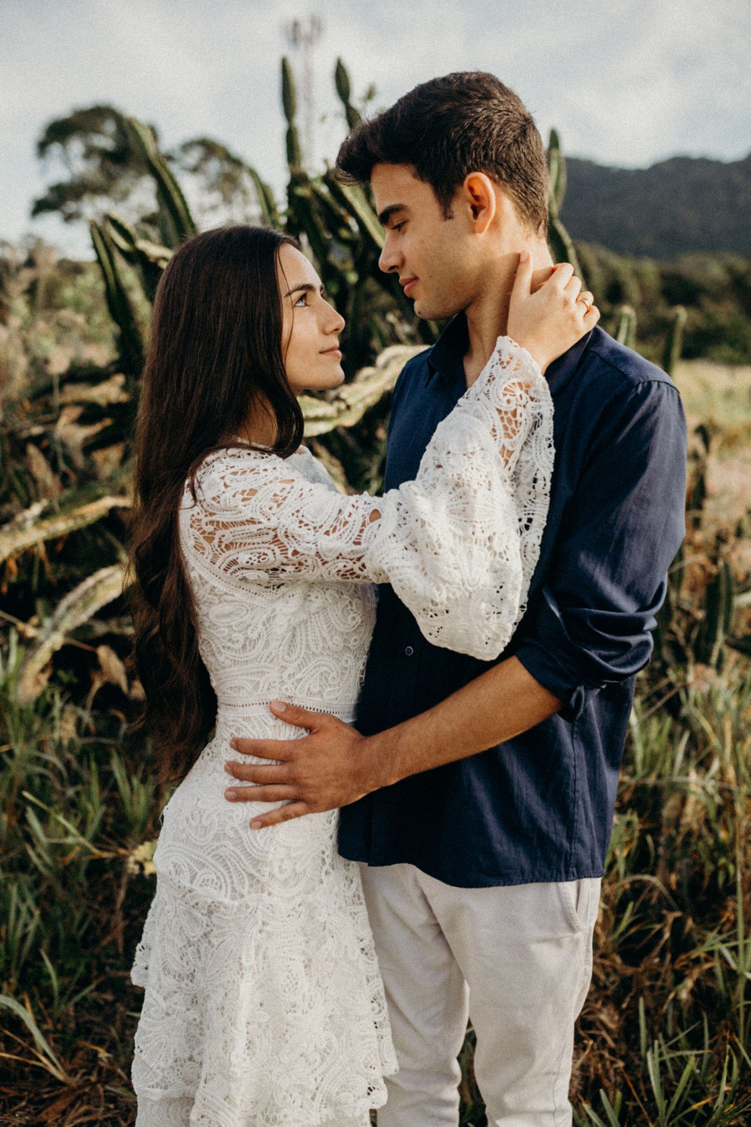 A couple in wedding attire share an intimate moment in a rural field at sunset.