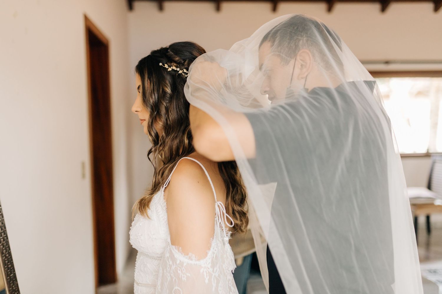 A bride getting her delicate white veil adjusted while wearing an elegant off-shoulder wedding dress.