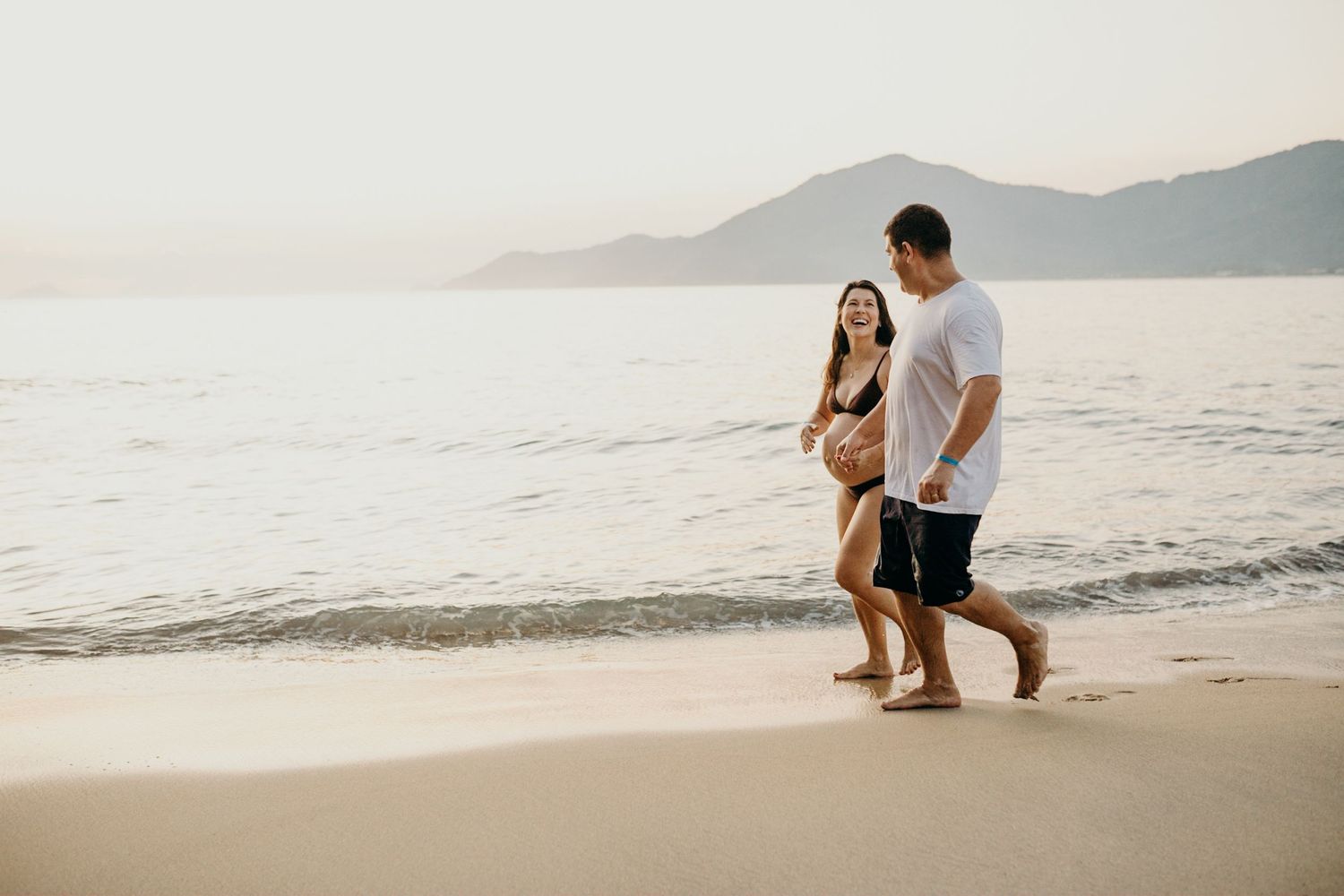 Long shot of people walking along a scenic beach with mountains in the distance.