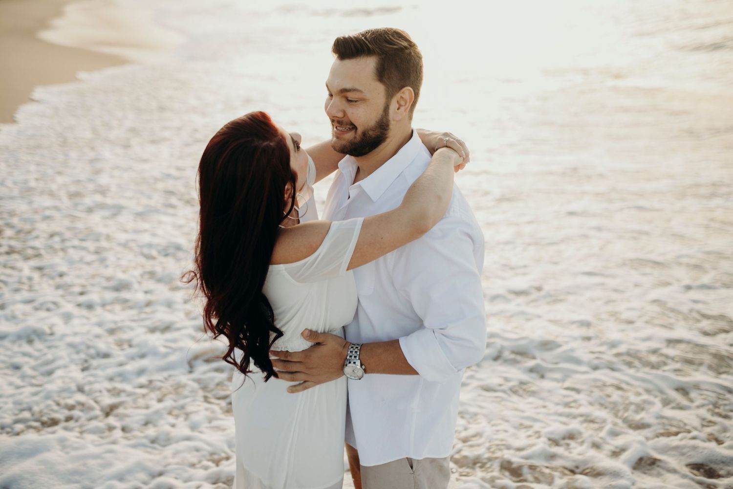 Two people share an intimate embrace on a sandy beach during golden hour.