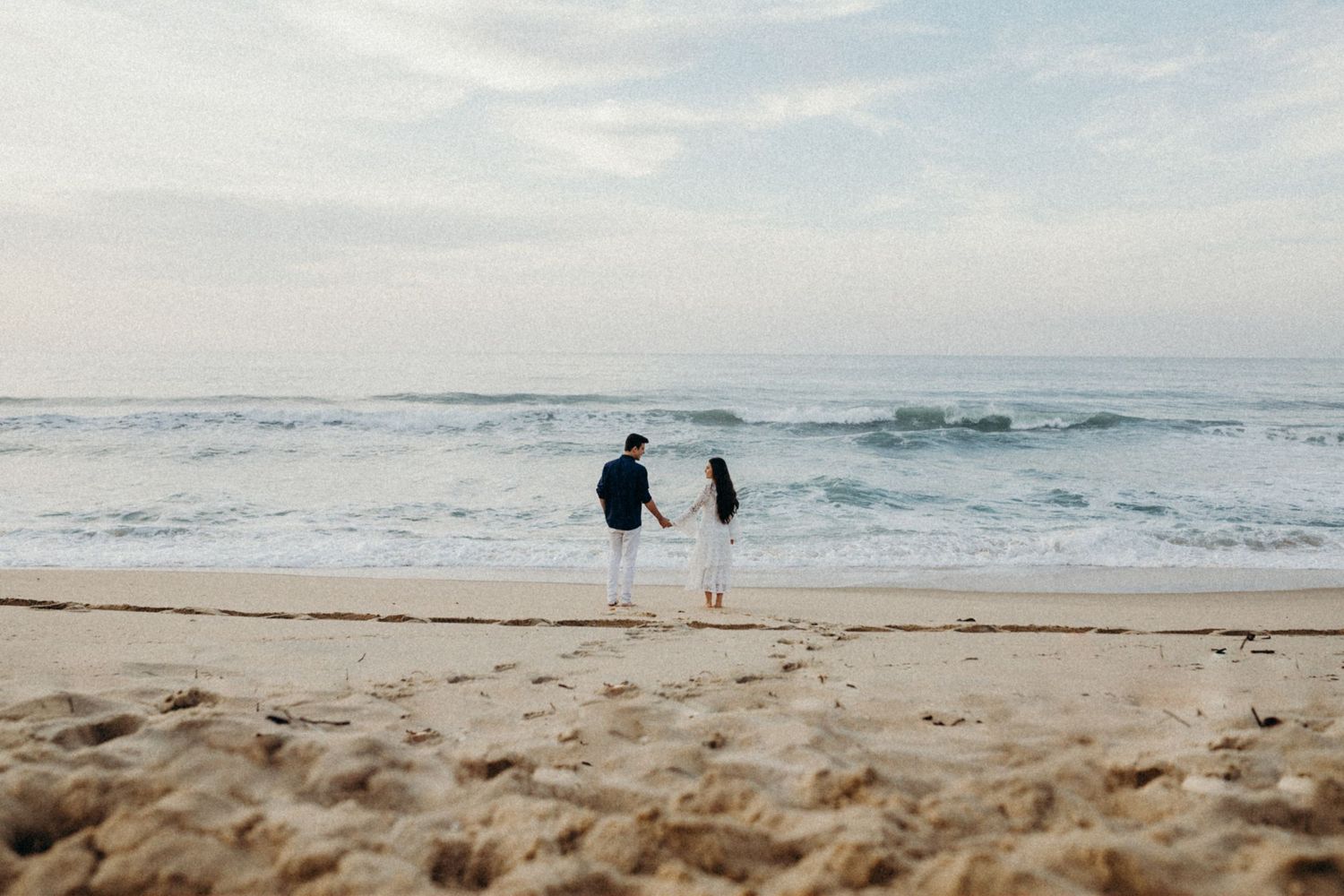 Silhouetted figures stand together on a sandy beach watching the ocean waves at dusk.